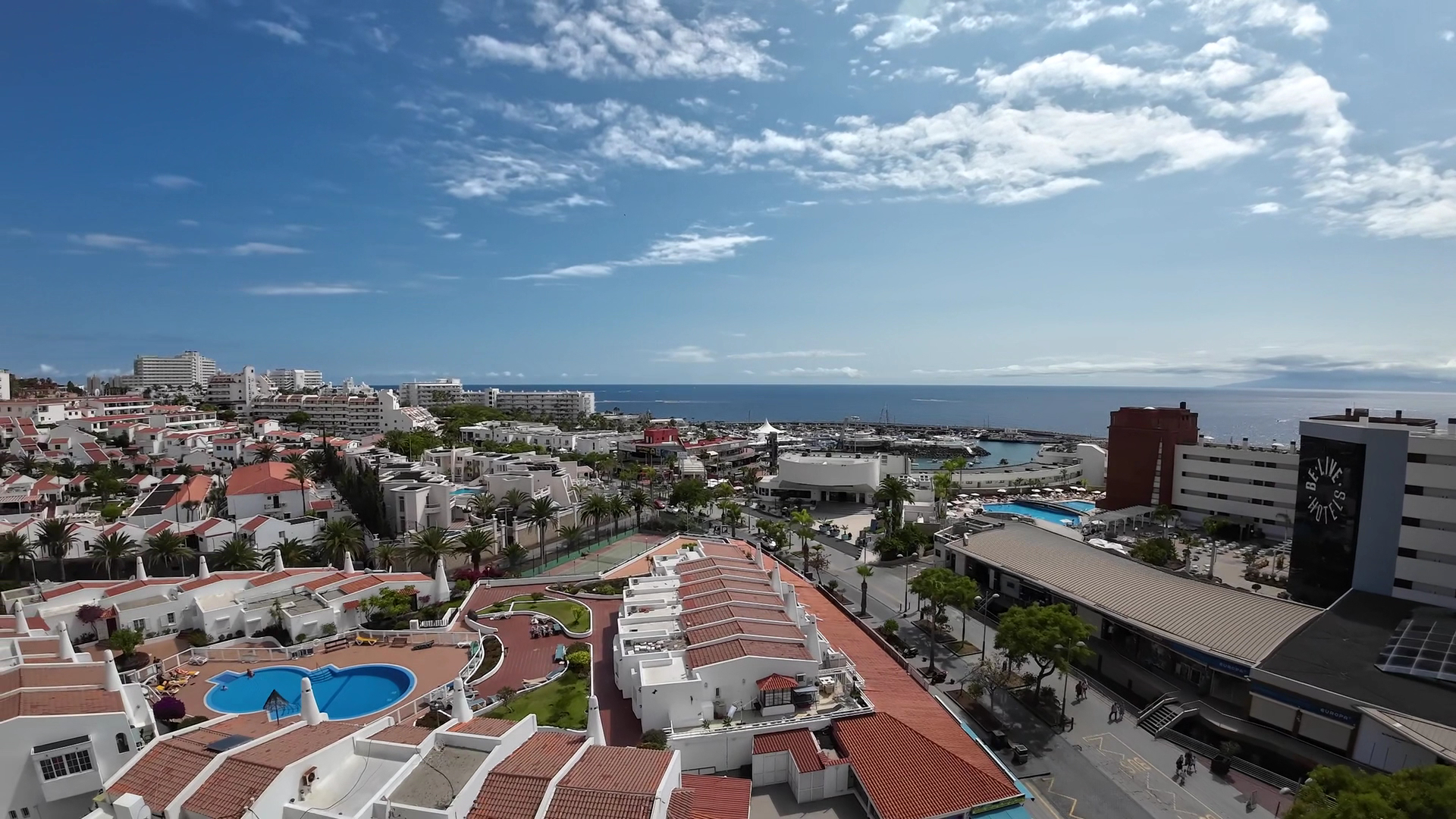 Hovima Santa Maria viesnīcas skats no augšas uz kūrorta apkaimi un okeāna piekrasti Tenerifē — redzami baseini, ēkas un osta