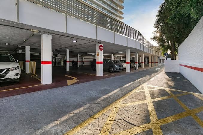 Viesnīcas Sol Torremolinos Don Pablo segtā autostāvvieta ar marķētām vietām un iebrauktuvi pie viesnīcas ēkas fasādes