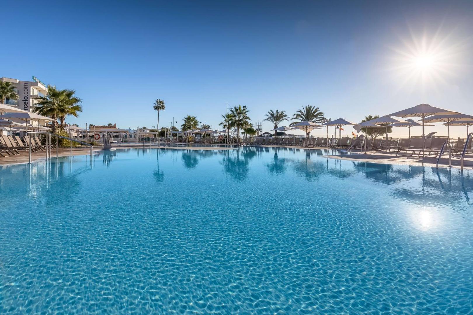 Occidental Torremolinos Playa plašais āra baseins saulainā dienā Kostadelsoilā — apkārt saulessargi, atpūtas krēsli un palmas zem skaidrām debesīm