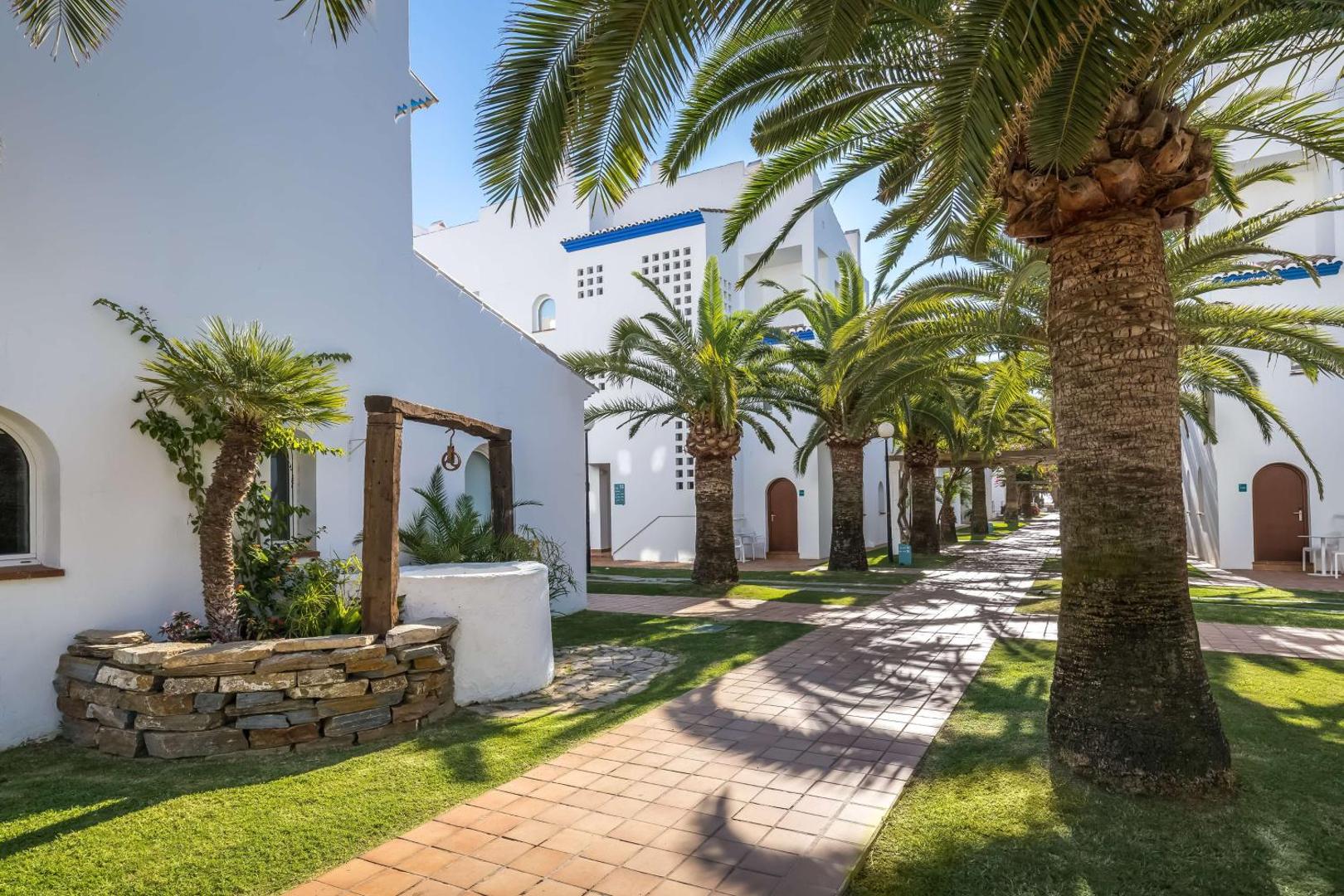 Viesnīcas Occidental Torremolinos Playa teritorija ar palmu alejām un gājēju celiņiem starp baltajiem numuru korpusiem.