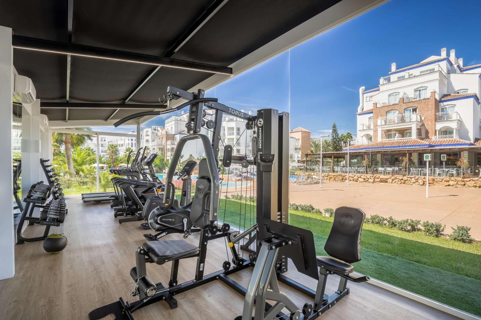 Occidental Torremolinos Playa mūsdienīga fitnesa zāle ar skatu uz viesnīcas teritoriju caur lieliem panorāmas logiem