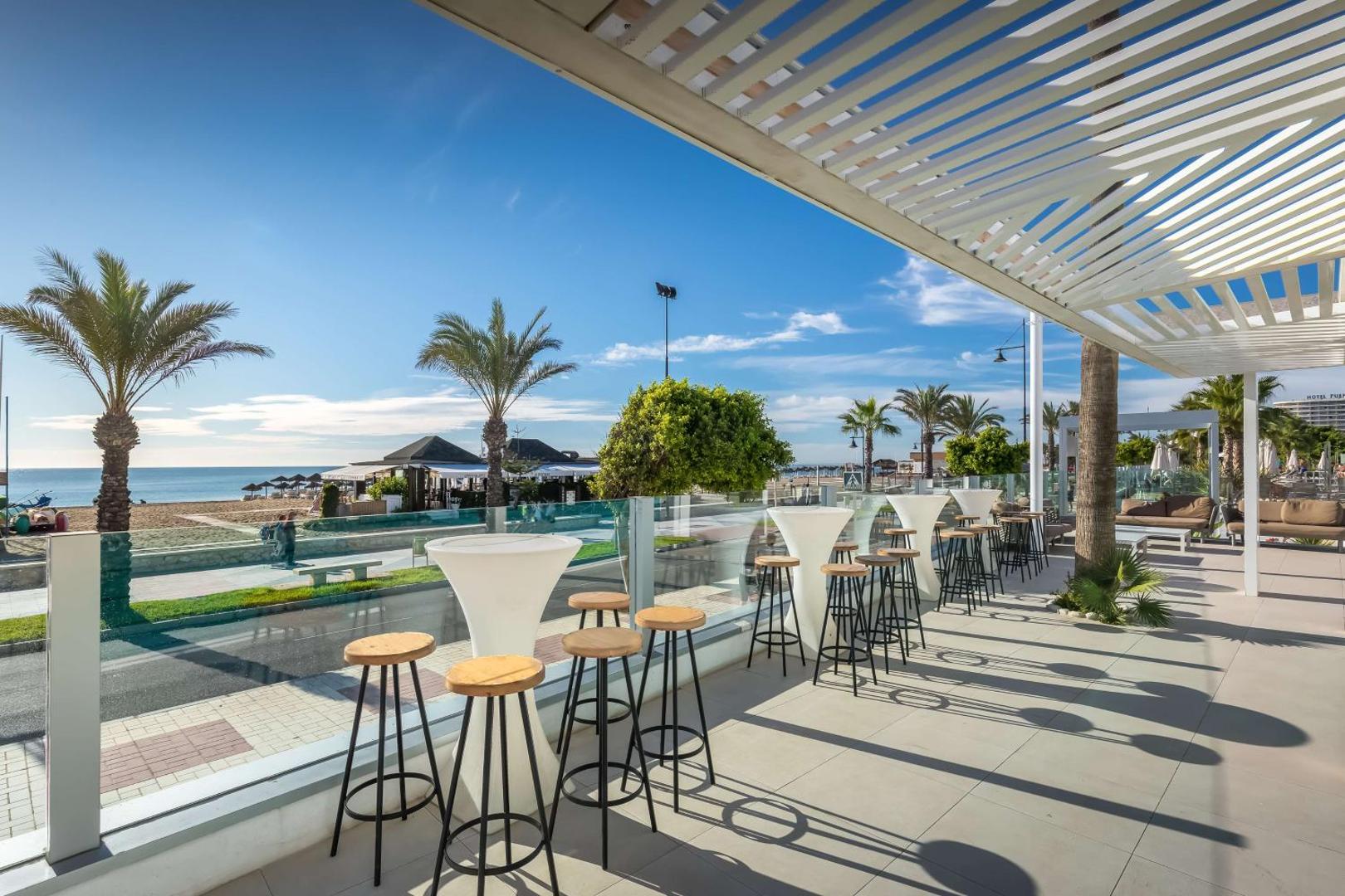 Occidental Torremolinos Playa āra terase ar bāra krēsliem un skatu uz Vidusjūru un pludmali — saulaina atpūtas vieta piekrastē
