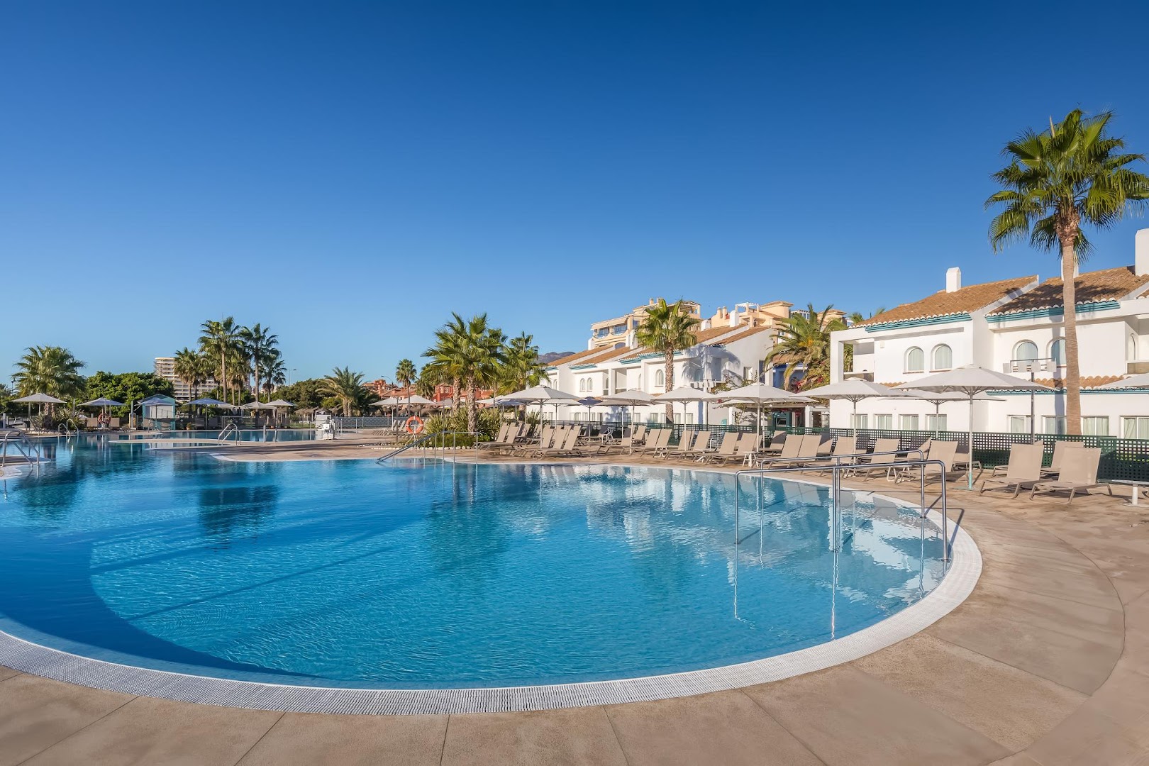 Occidental Torremolinos Playa baseina zona ar baltām ēkām un palmām — zili ūdeņi un sakopta teritorija atpūtai Spānijas dienvidos