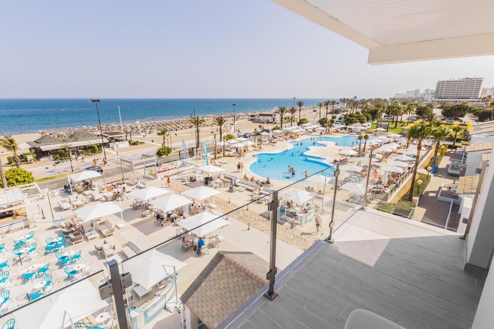 Skats no Occidental Torremolinos Playa balkona uz viesnīcas baseinu kompleksu, atpūtas zonu ar saulessargiem un blakus esošo pludmali.