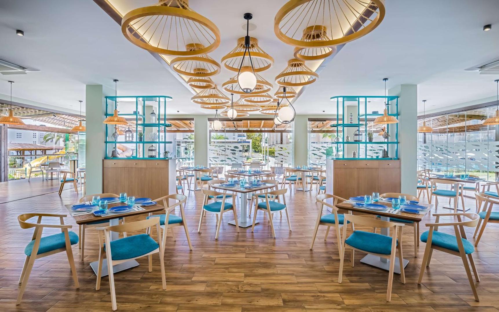 Occidental Torremolinos Playa restorāns ar modernām koka mēbelēm, ziliem akcentiem un unikāliem dizaina gaismekļiem pie griestiem Spānijas piekrastē.