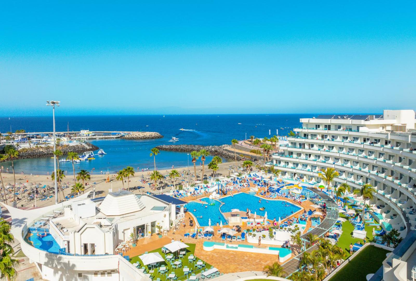 Hovima La Pinta viesnīcas ēka un baseinu zona pie okeāna krasta Kostadeje, Tenerifē — skats no augšas uz pludmali un ostu