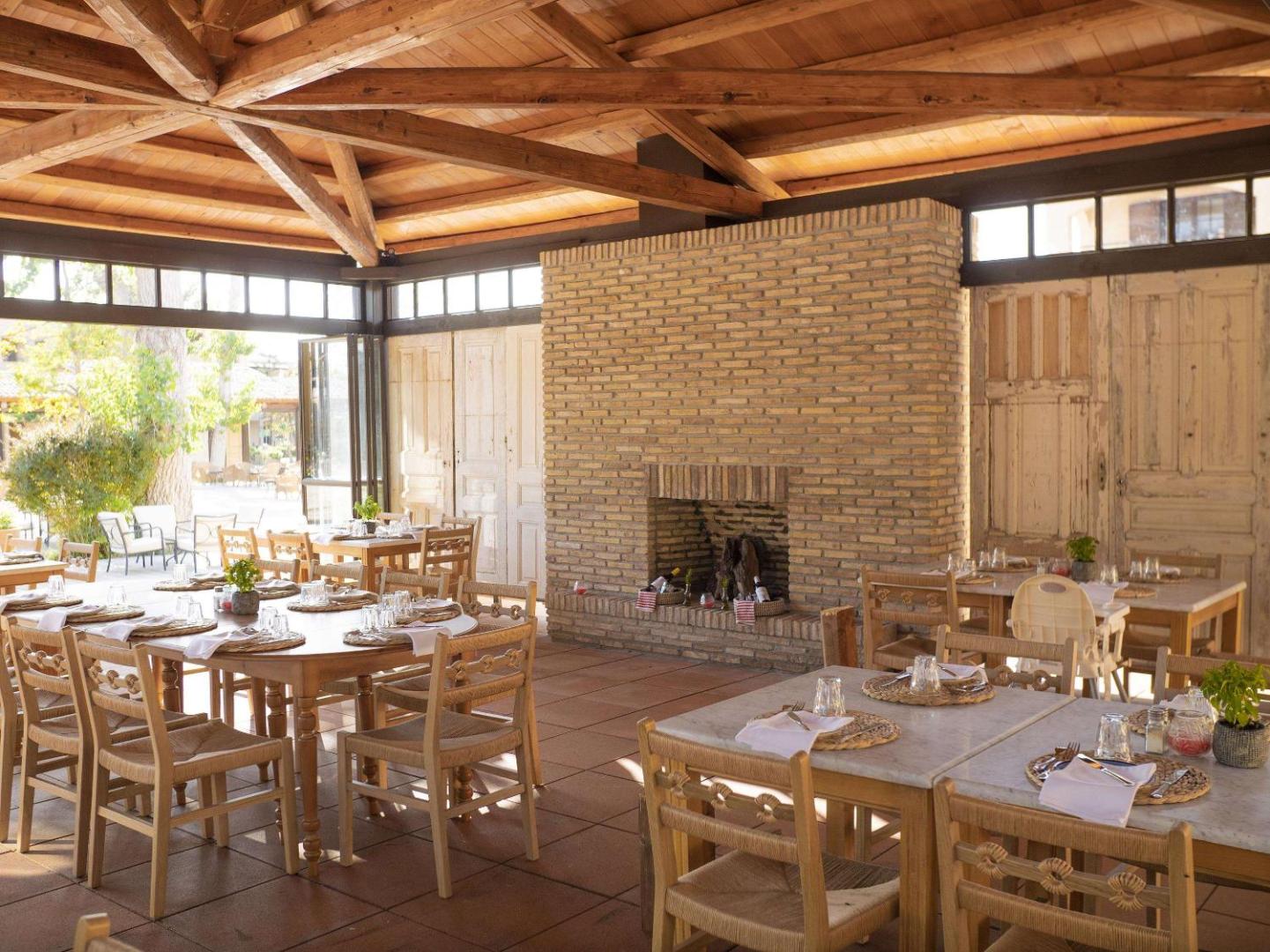 Grecotel Costa Botanica restorāns ar koka siju griestiem un lielu ķieģeļu kamīnu — mājīga ēdamzāle ar koka mēbelēm