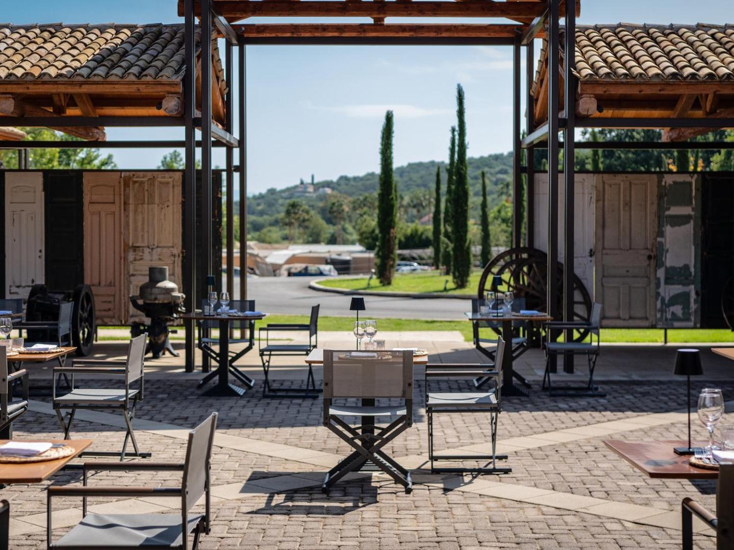 Grecotel Costa Botanica āra terase ar galdiņiem un skatu uz kalniem un cipresēm — eleganta atpūtas zona Korfu piekrastē