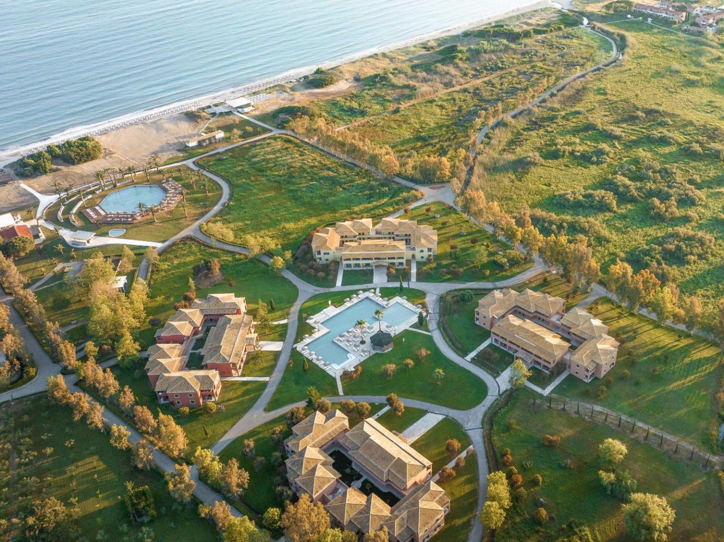 Grecotel Costa Botanica plašā teritorija no gaisa — redzami vairāki numuru korpusi, baseini un tieša piekļuve smilšu pludmalei