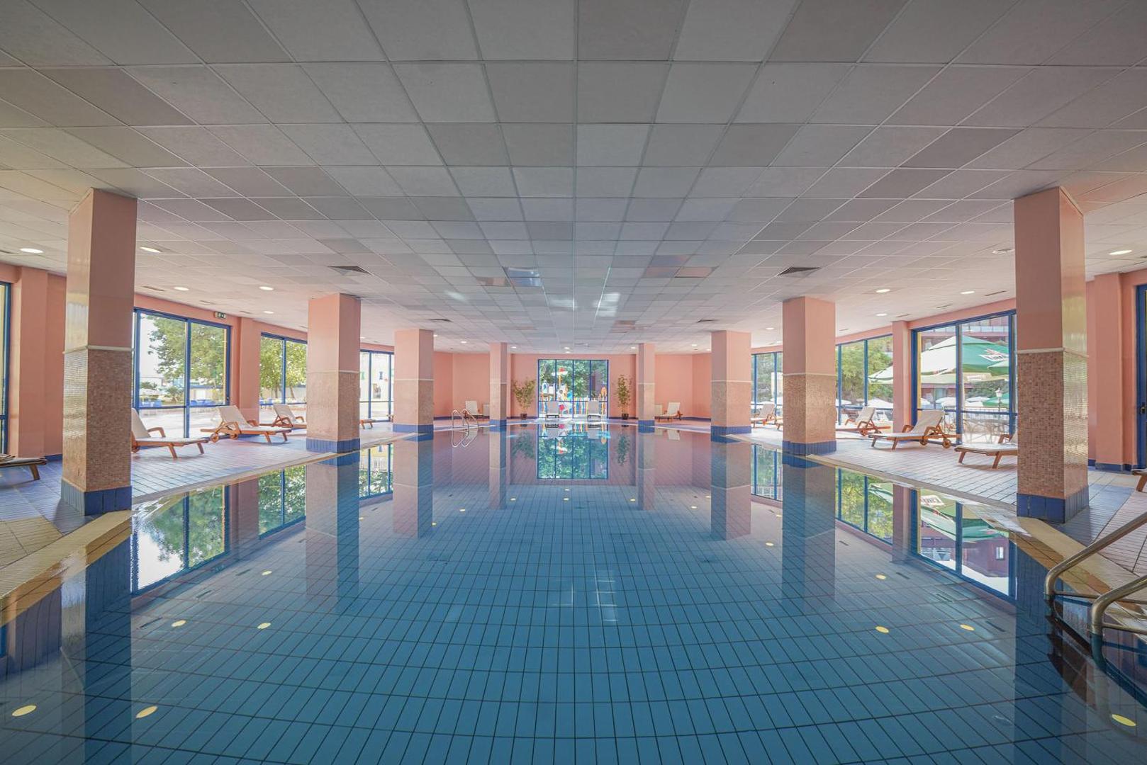 Grifid Hotel Arabella iekštelpu baseins ar apsildāmu ūdeni, atpūtas krēsliem un lieliem logiem uz dārza pusi