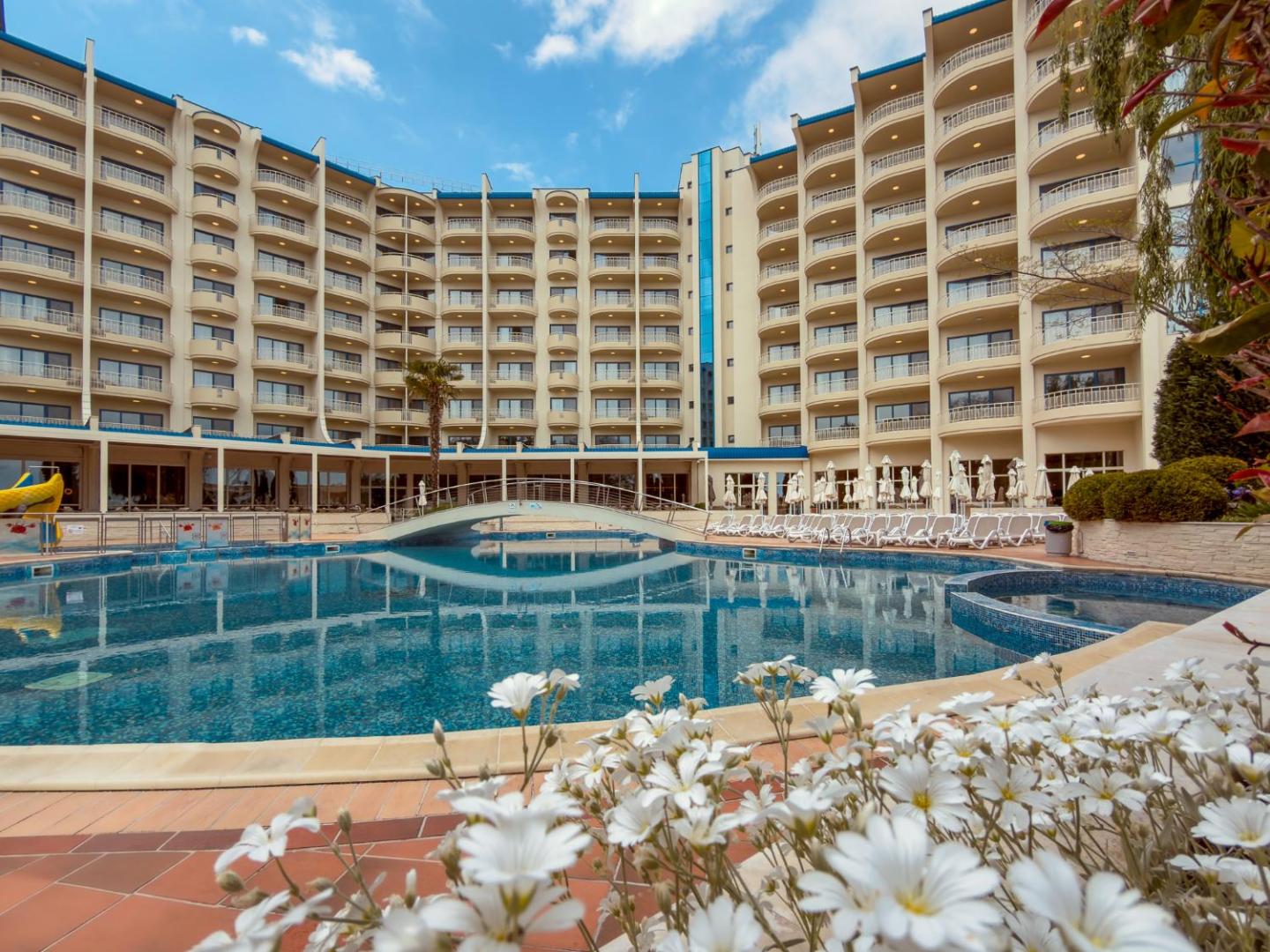 Grifid Hotel Arabella centrālais baseins ar dekoratīvu tiltiņu un ziediem priekšplānā — skats uz daudzstāvu viesnīcas korpusu