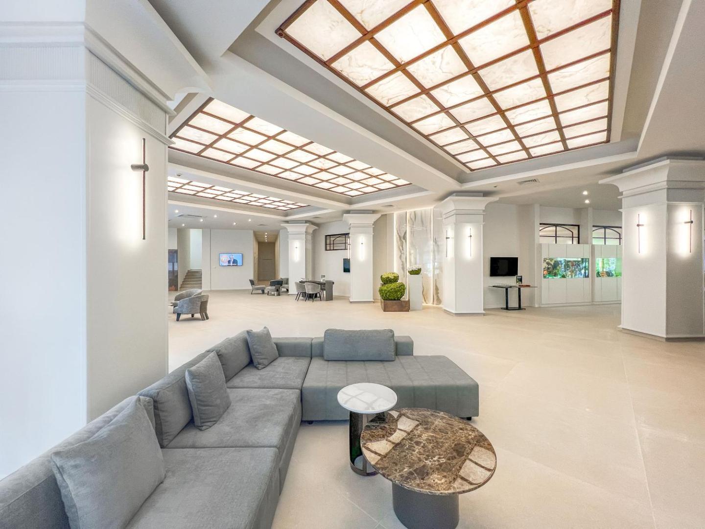 Grifid Club Hotel Bolero plašais lobby ar modernu dīvānu, akvāriju un stilīgu apgaismojumu viesnīcas reģistratūras zonā