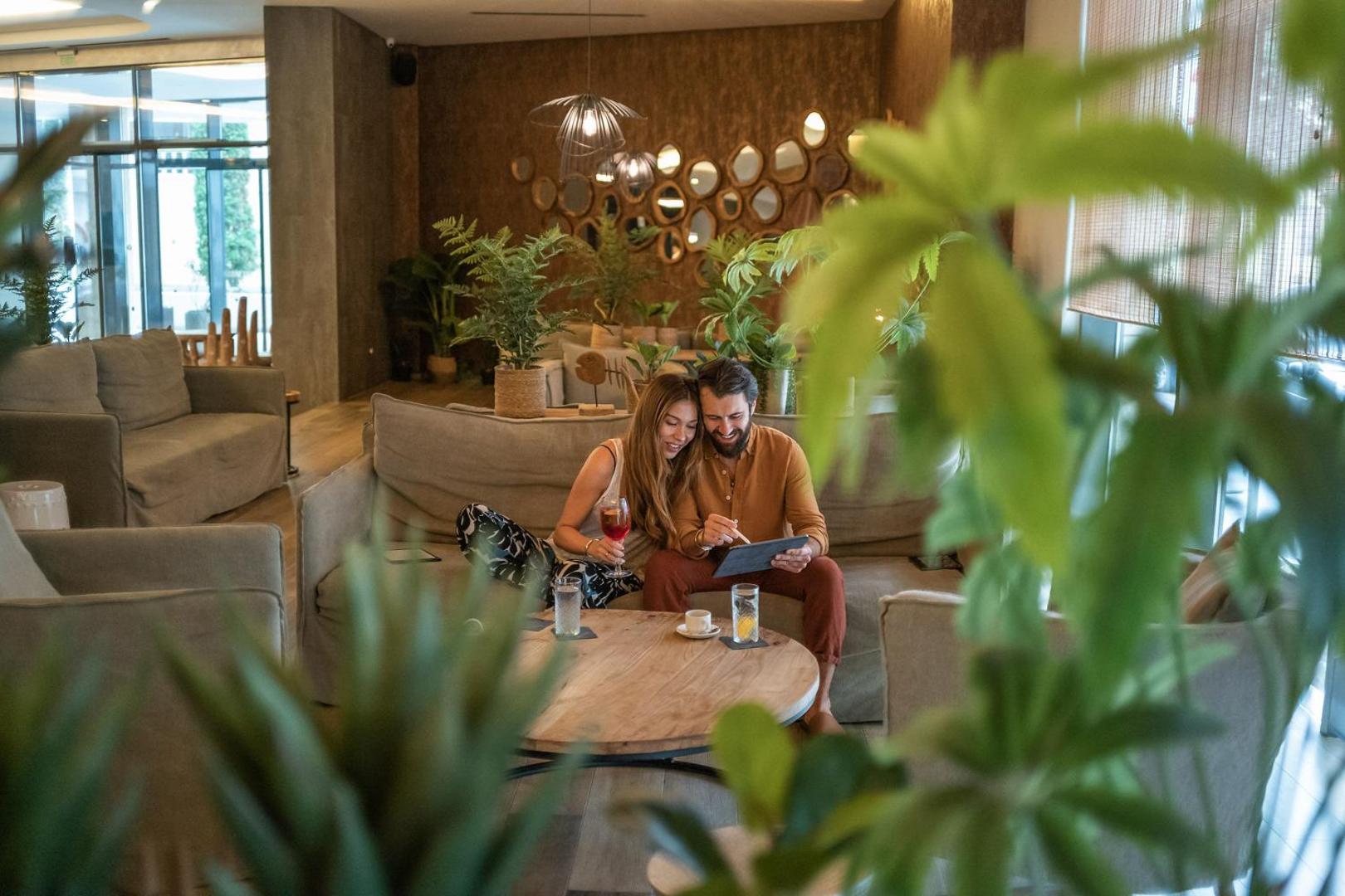 Pāris atpūšas GRIFID Vistamar Hotel lobby zonā uz mīkstiem dīvāniem, malkojot dzērienus un izmantojot planšetdatoru