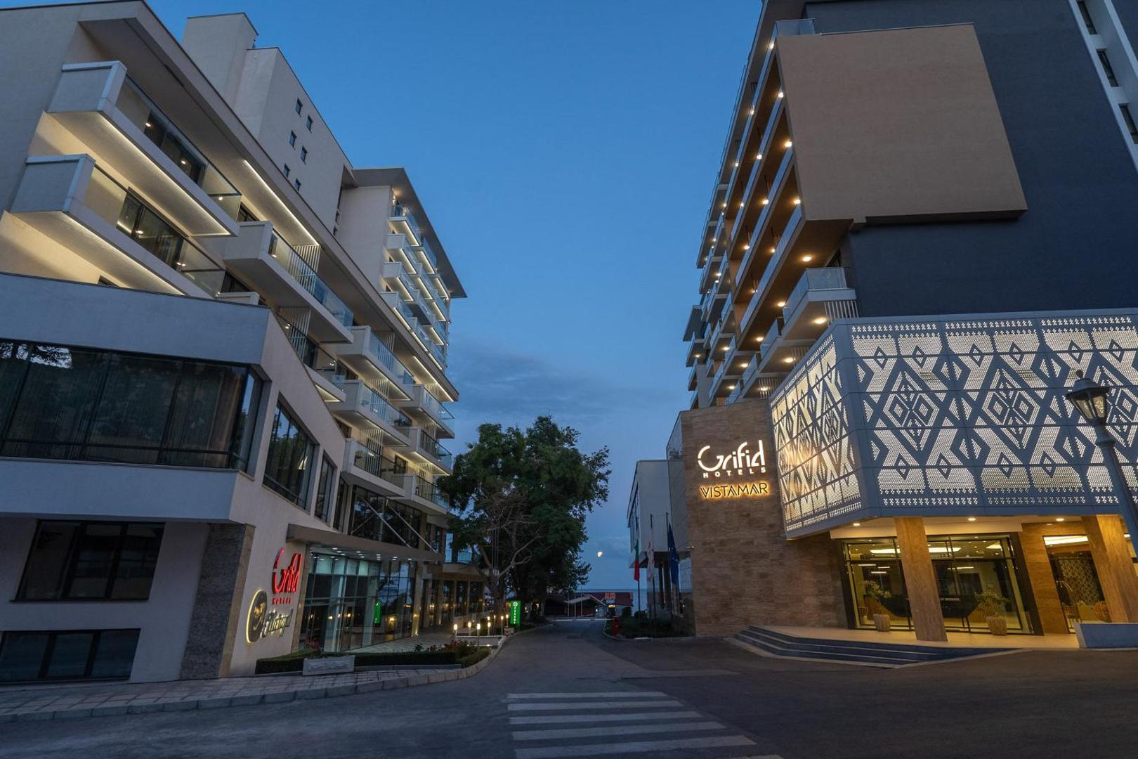 GRIFID Vistamar Hotel ieeja un modernā fasāde vakara apgaismojumā — arhitektūra un viesnīcas logo Zelta Smilšu kūrortā