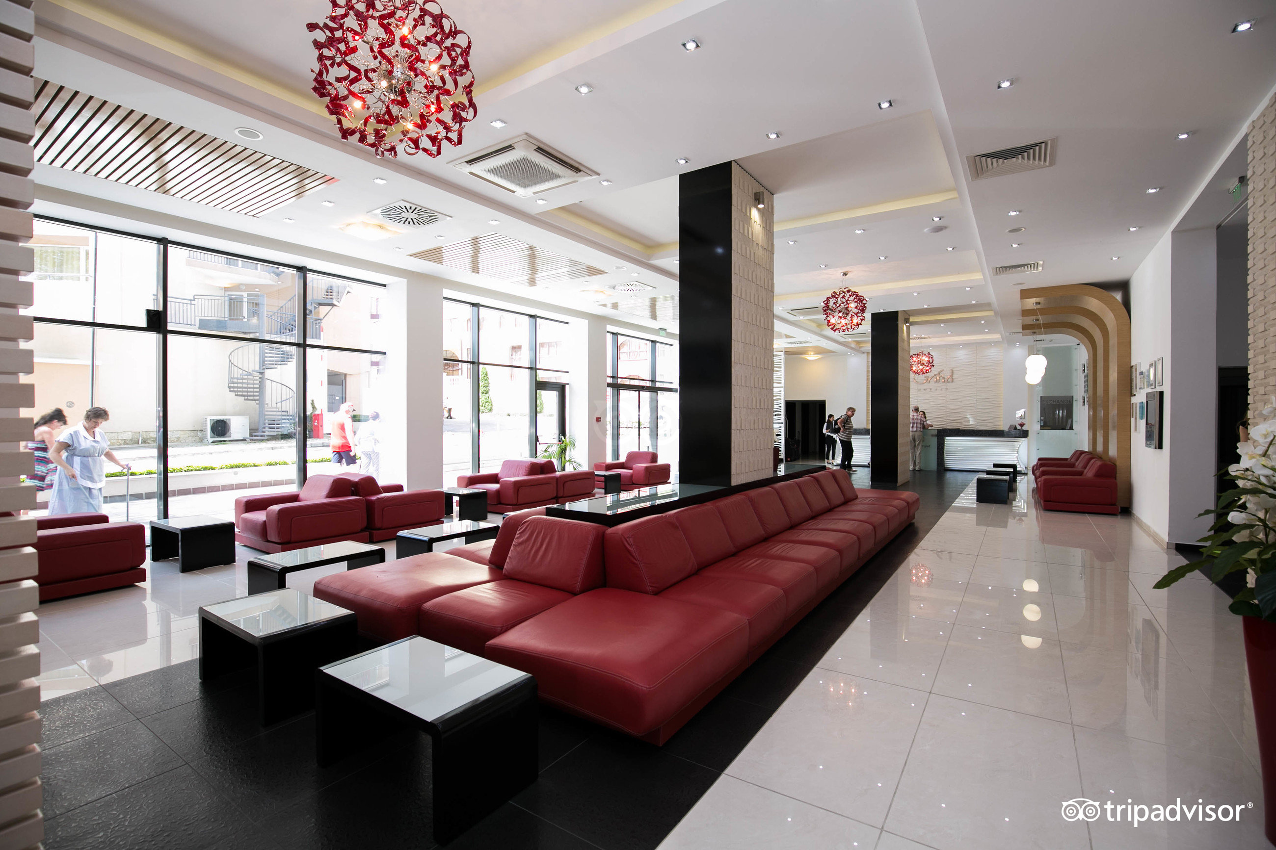 GRIFID Metropol Hotel plašais lobby ar moderniem sarkaniem dīvāniem, lieliem logiem un gaišu flīžu grīdu