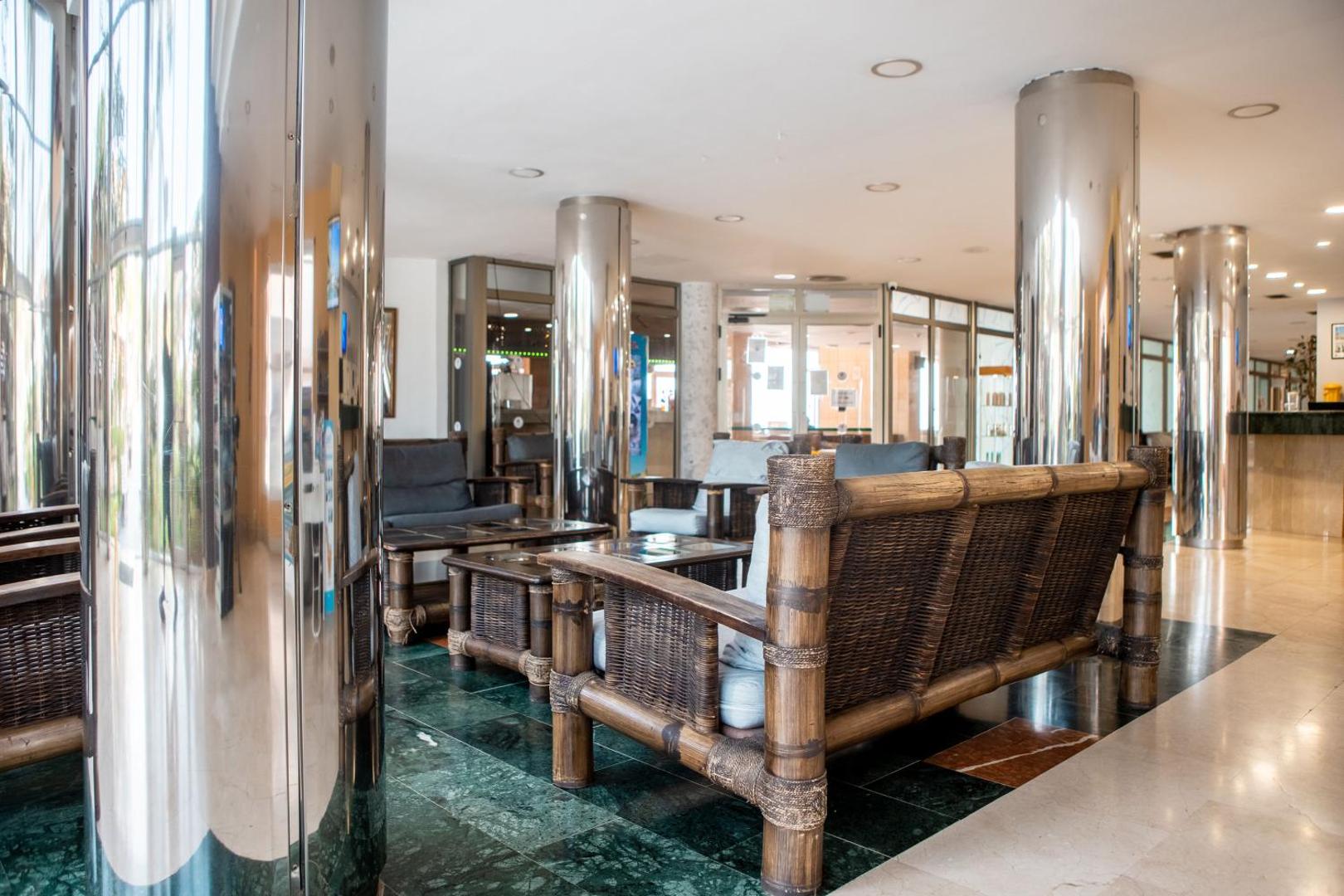 Villa De Adeje Beach viesnīcas lobby zona ar bambusa mēbelēm, mīkstiem krēsliem un spīdīgām metāla kolonnām Tenerifē