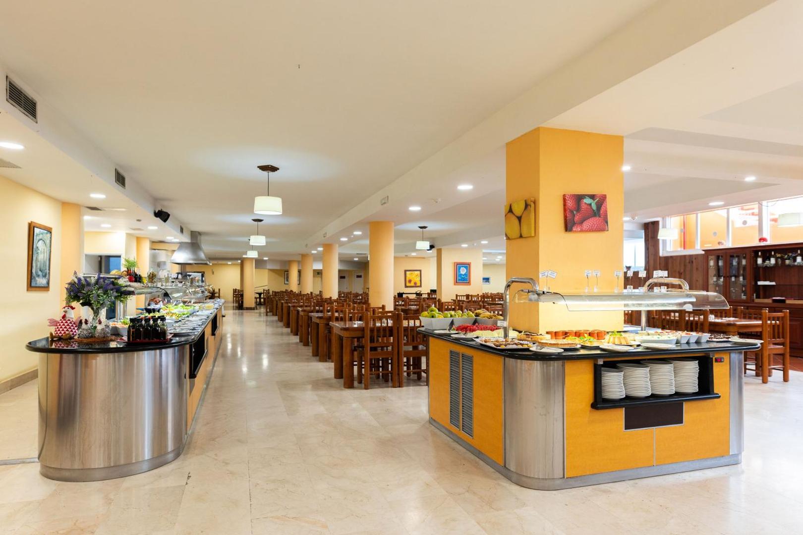 Viesnīcas Villa De Adeje Beach plašā restorāna zāle Tenerifē ar bufetes tipa galdiem, koka mēbelēm un gaišu interjeru