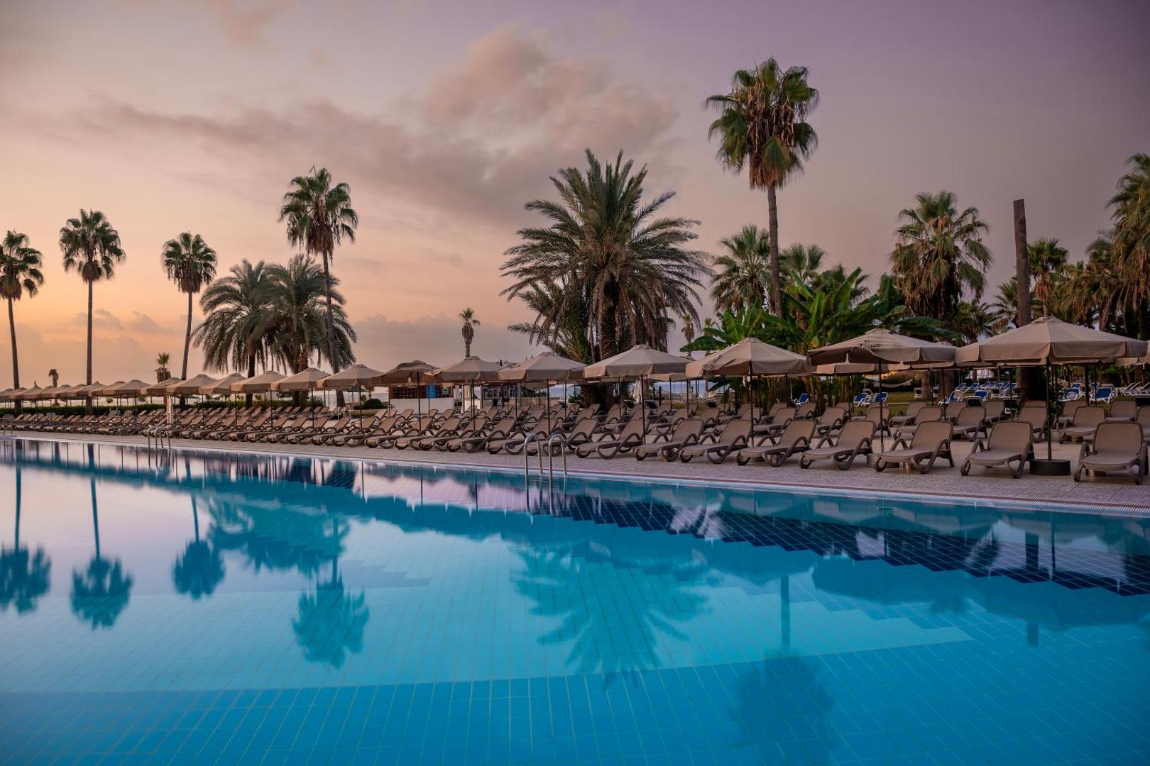 Adora Hotel & Resort baseina zona krēslas stundā ar atspulgiem ūdenī, saulessargiem un palmām piekrastes kūrortā