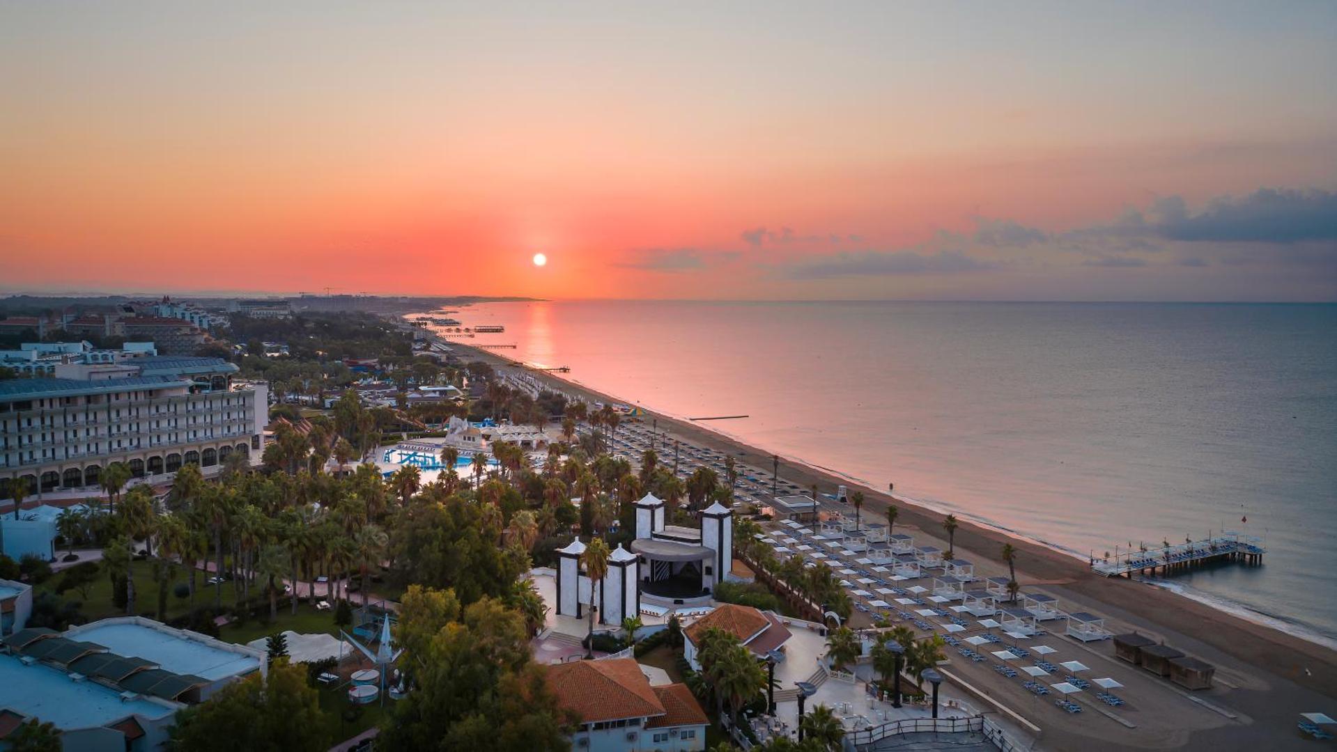 Adora Hotel & Resort saulrieta panorāma Belekā pie Vidusjūras — skats no augšas uz viesnīcas teritoriju, pludmali un koka piestātni