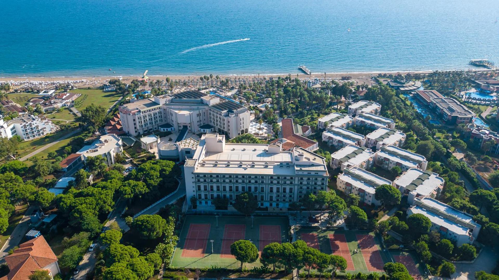 Adora Hotel & Resort panorāmas skats no putna lidojuma Belekā — viesnīcas korpusi, tenisa korti un plaša pludmale pie Vidusjūras