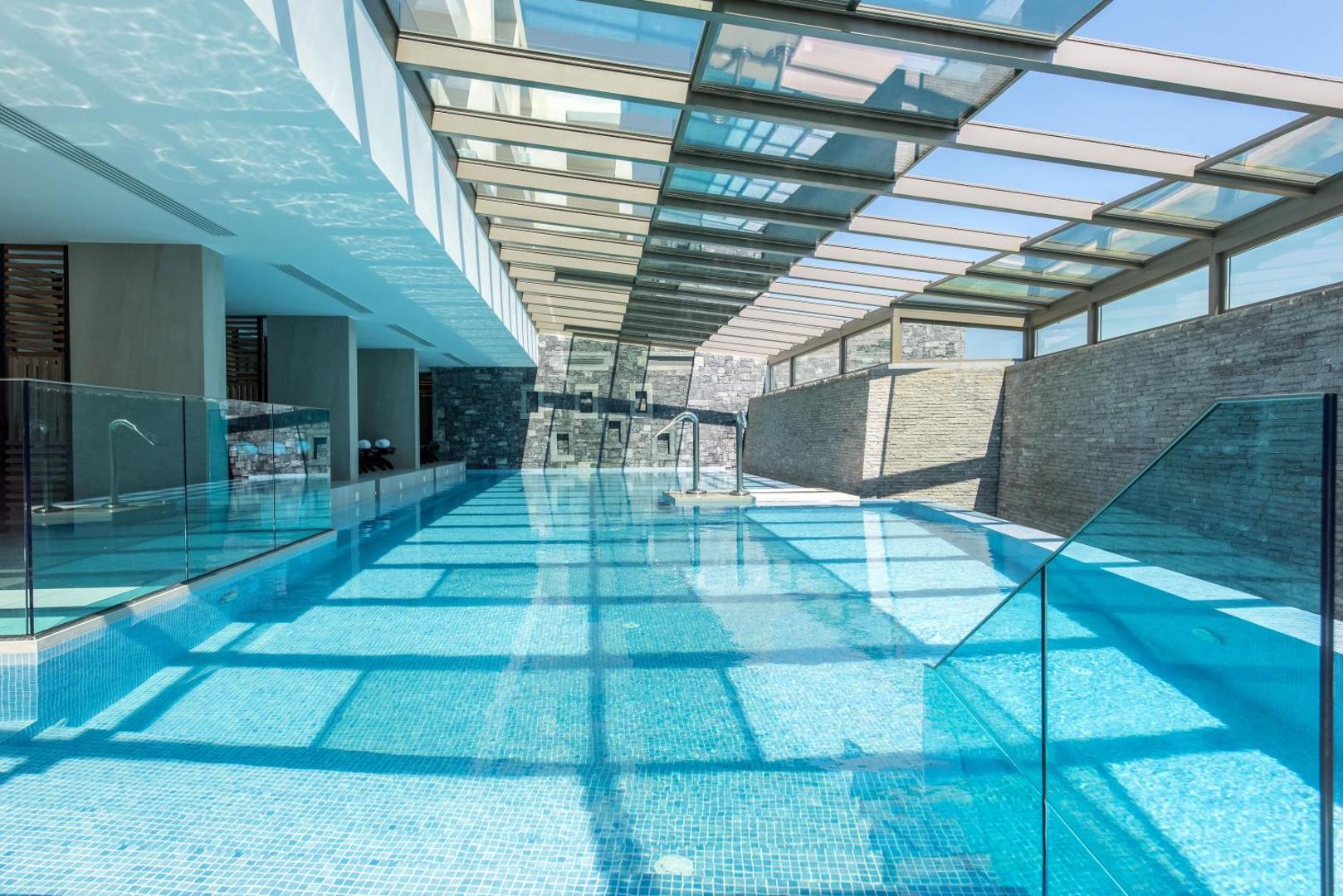 Nana Princess Suites Villas & Spa iekštelpu baseins ar stikla jumtu un akmens sienām — moderna spa zona relaksācijai