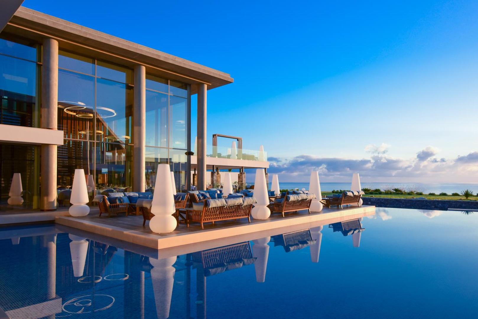 Nana Princess Suites Villas & Spa āra terase ar atpūtas dīvāniem pie baseina saulrietā Hersonisā, Krētā — skats uz jūru