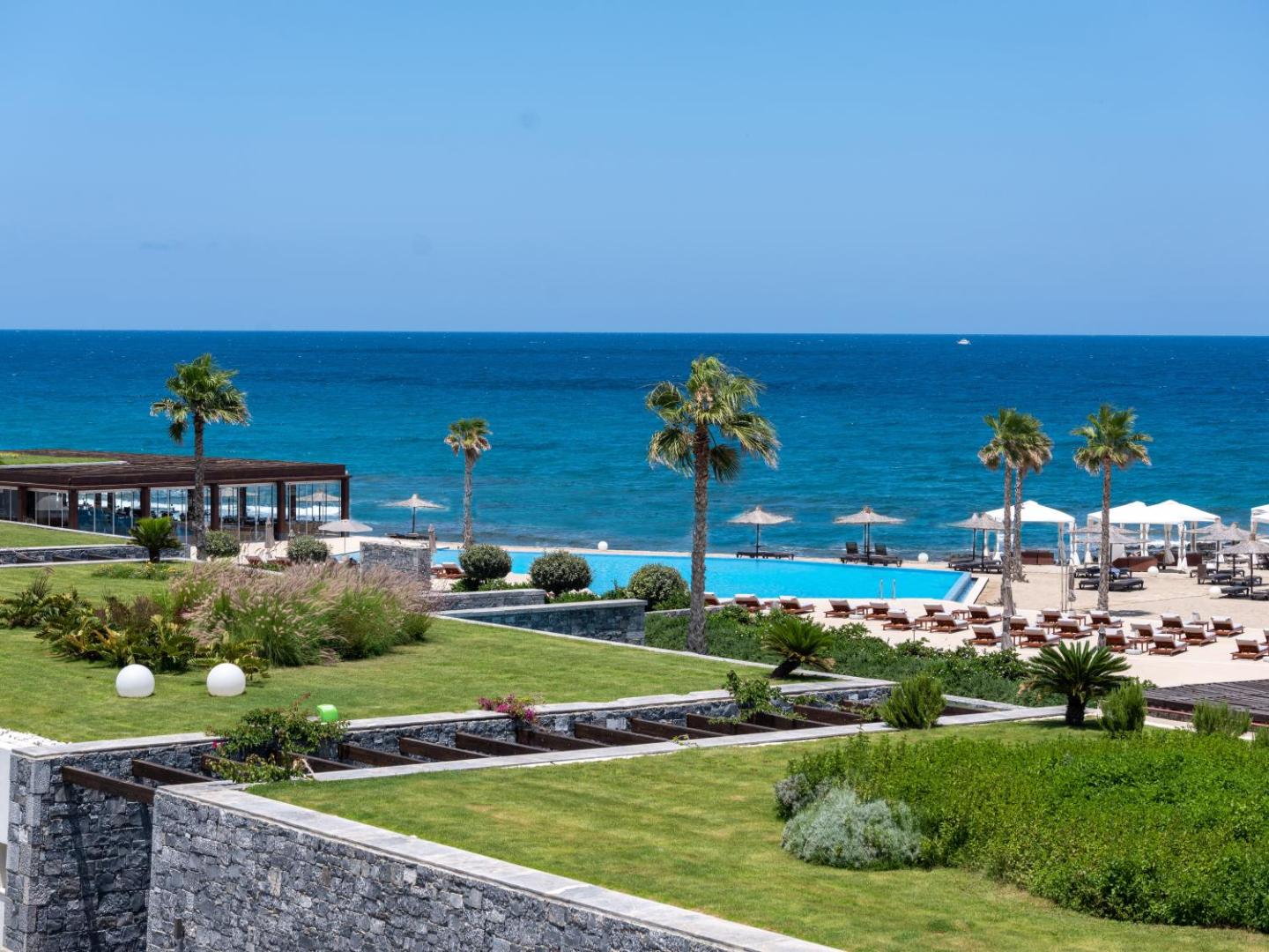 Nana Princess Suites Villas & Spa skats no augšas uz āra baseinu, koptu zālienu un zilo Vidusjūru Hersonisā, Krētā