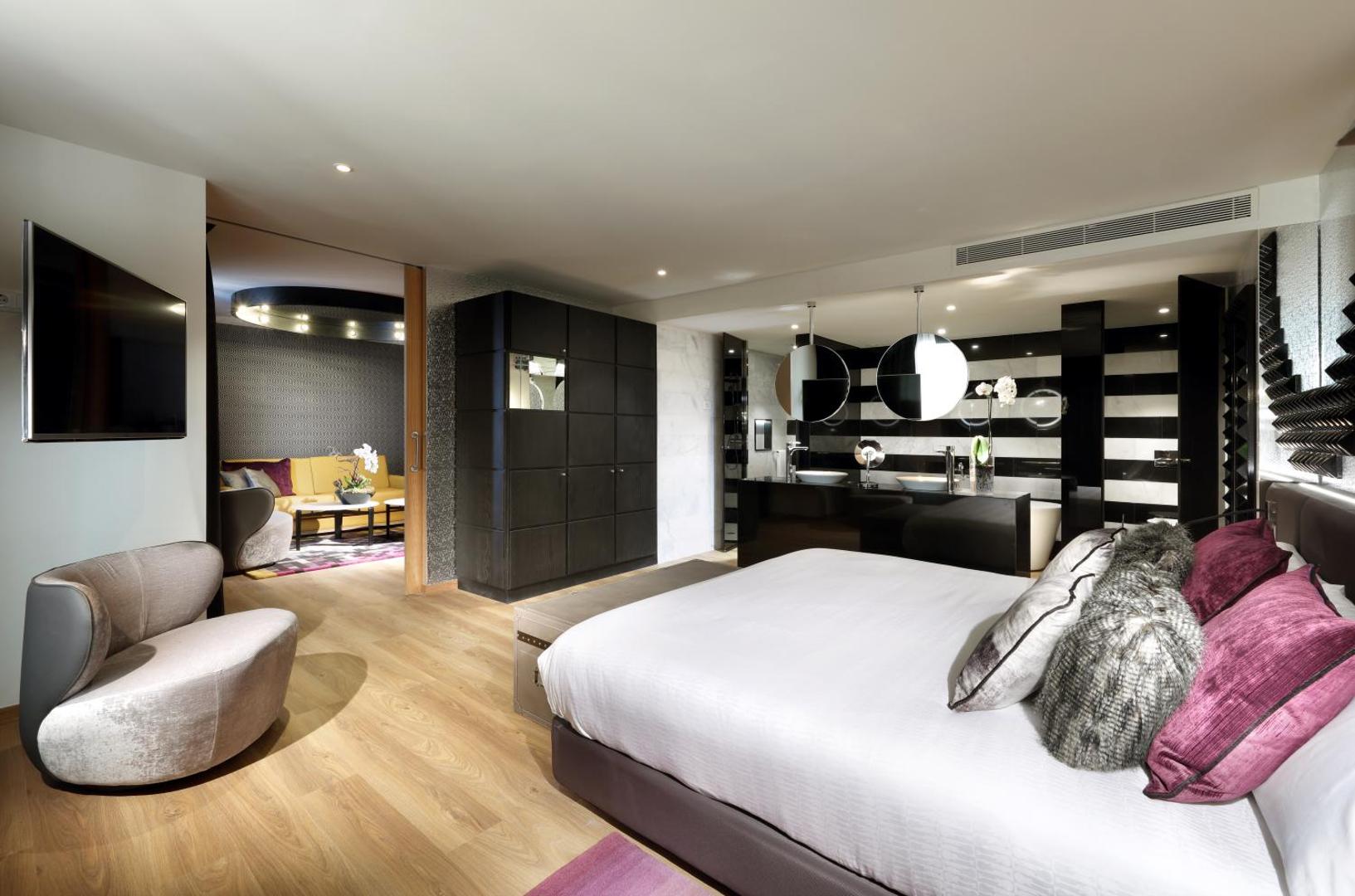 Hard Rock Hotel Tenerife luksusa numura interjers ar atsevišķu atpūtas zonu, dīvānu un stilīgu melnbaltu vannas istabas dizainu.