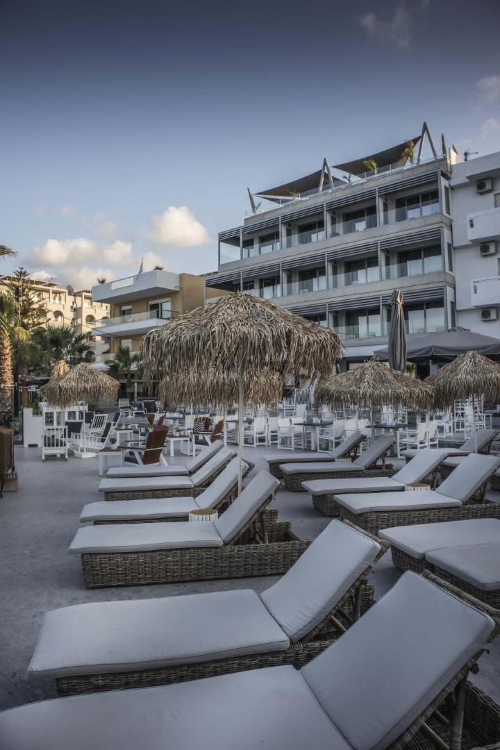 Glaros Royal Beach viesnīcas ēka un sauļošanās terase ar pītiem zviļņiem un salmu saulessargiem Hersonisas kūrortā, Krētā