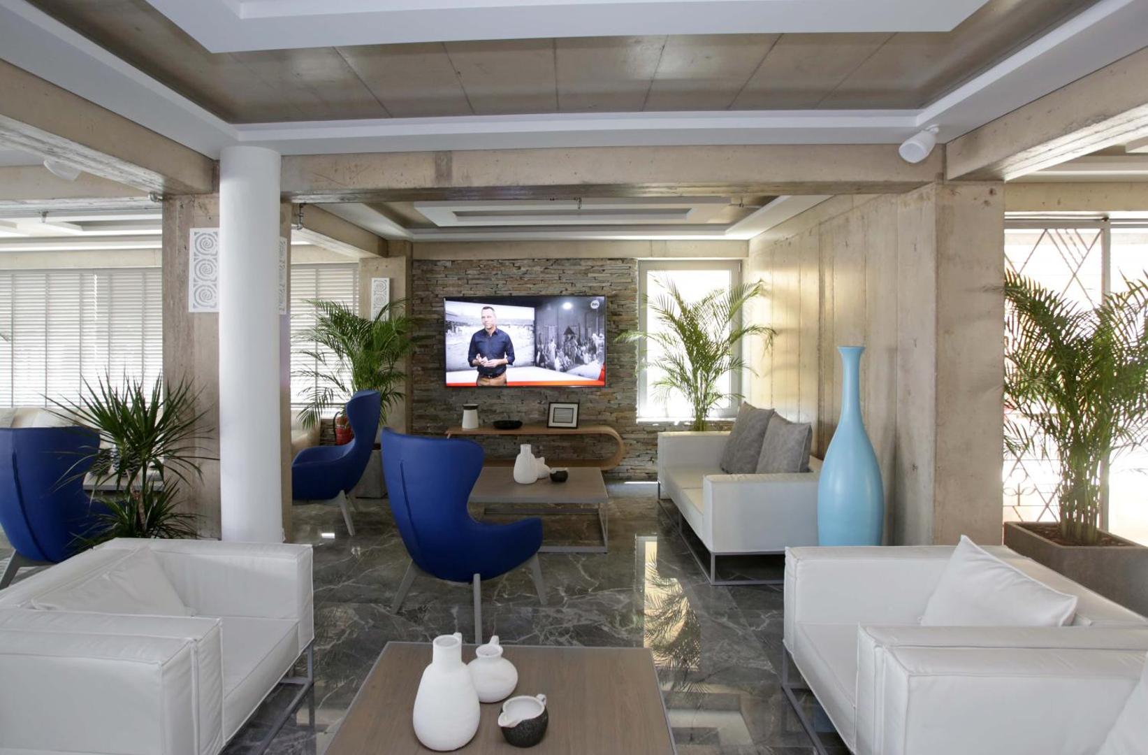 Glaros Royal Beach viesnīcas lobby atpūtas zona ar ziliem dizaina krēsliem, baltiem dīvāniem un marmora grīdu