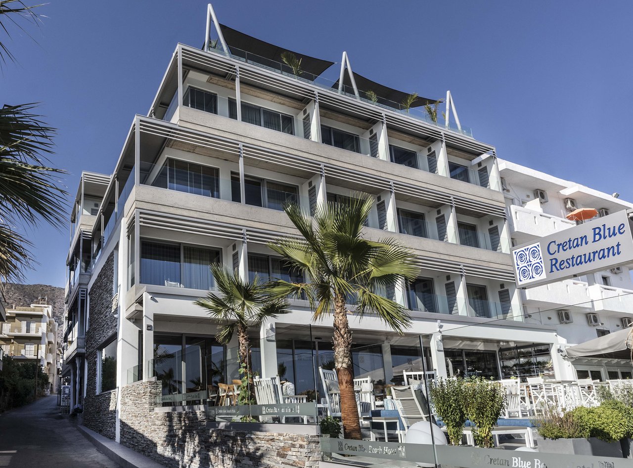 Glaros Royal Beach viesnīcas modernā fasāde un Cretan Blue restorāna ieeja Hersonisā ar palmām un āra mēbelēm