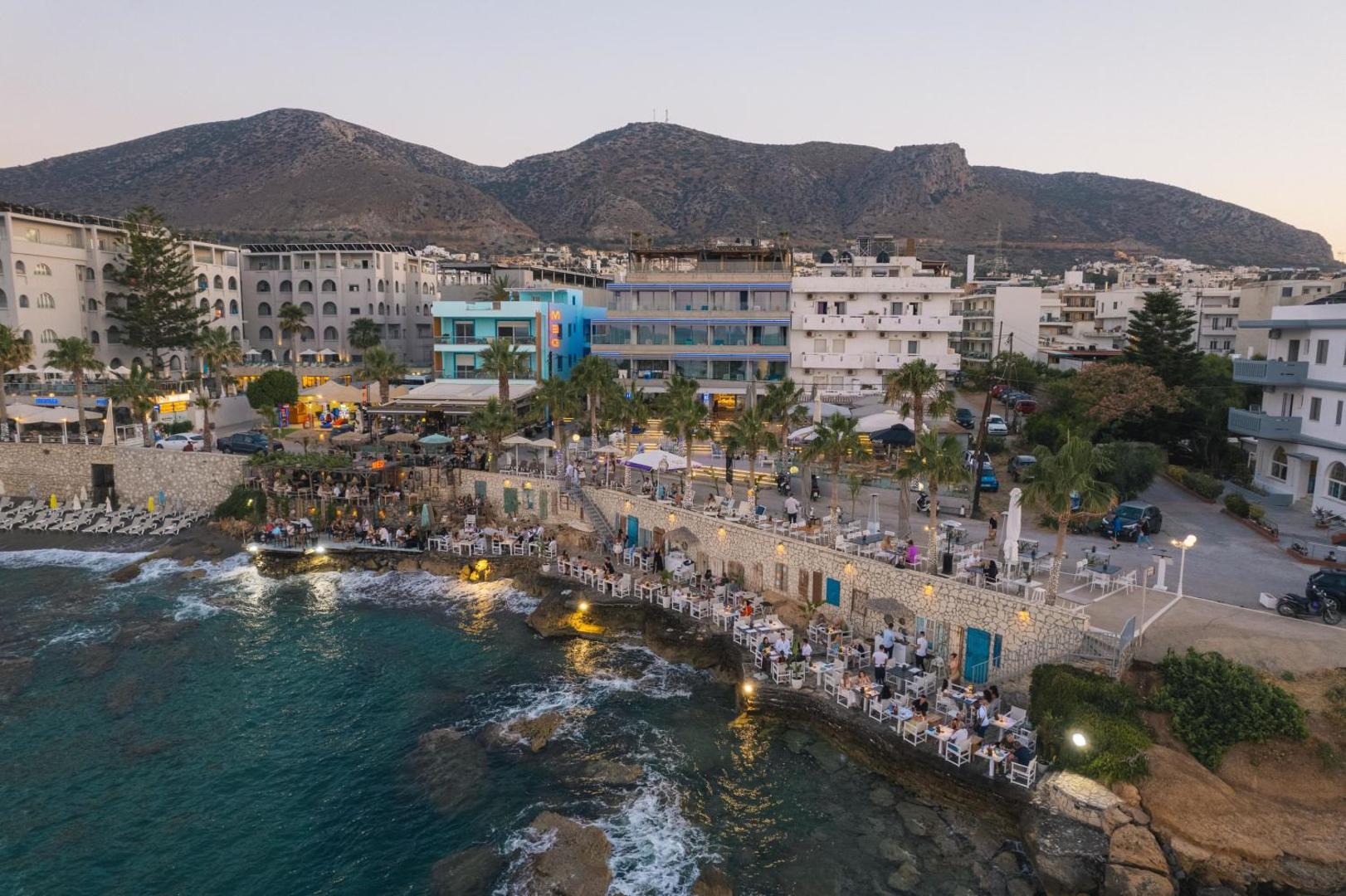 Glaros Royal Beach viesnīcas skats no putna lidojuma vakarā Hersonisā, Krētā — piekrastes restorāni un bāri pie pašas jūras