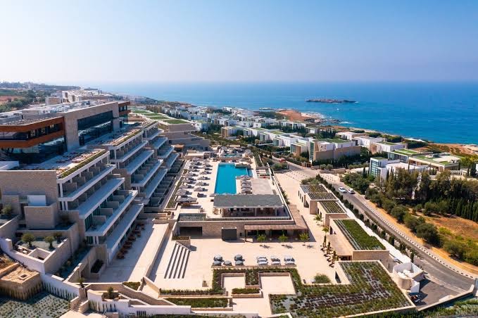 Cap St Georges Hotel & Resort panorāmas skats no putna lidojuma Pafosā, Kiprā — plaša teritorija ar baseiniem, terasēm un Vidusjūras piekrasti