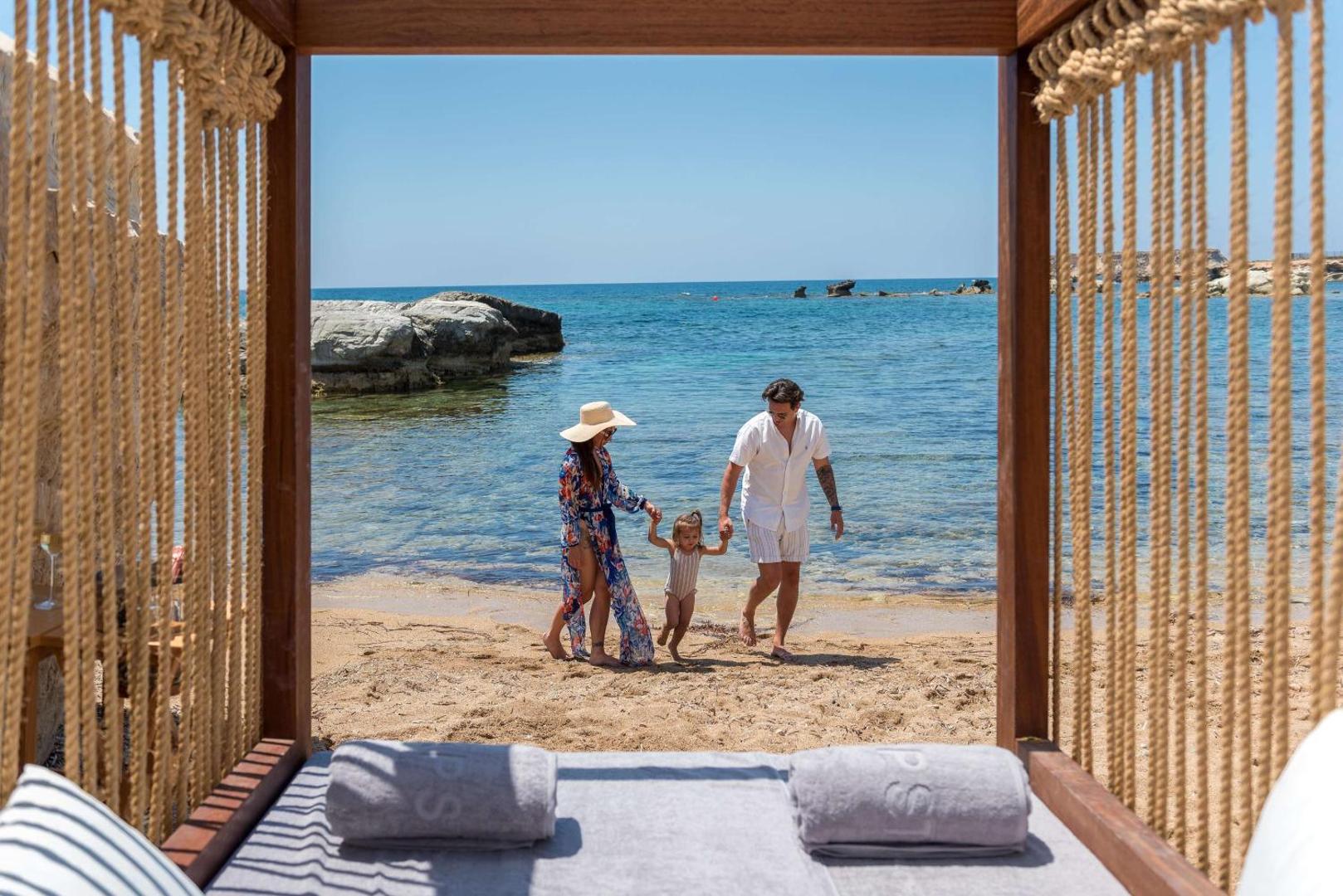 Ģimene pastaigājas Cap St Georges Hotel & Resort pludmalē, skats no atpūtas bungalo puses uz jūru