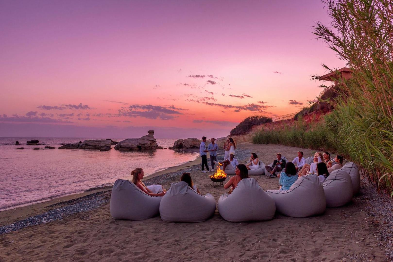 Cap St Georges Hotel & Resort viesi bauda vakaru pie ugunskura pludmalē saulrieta laikā Pafas reģionā, Kiprā