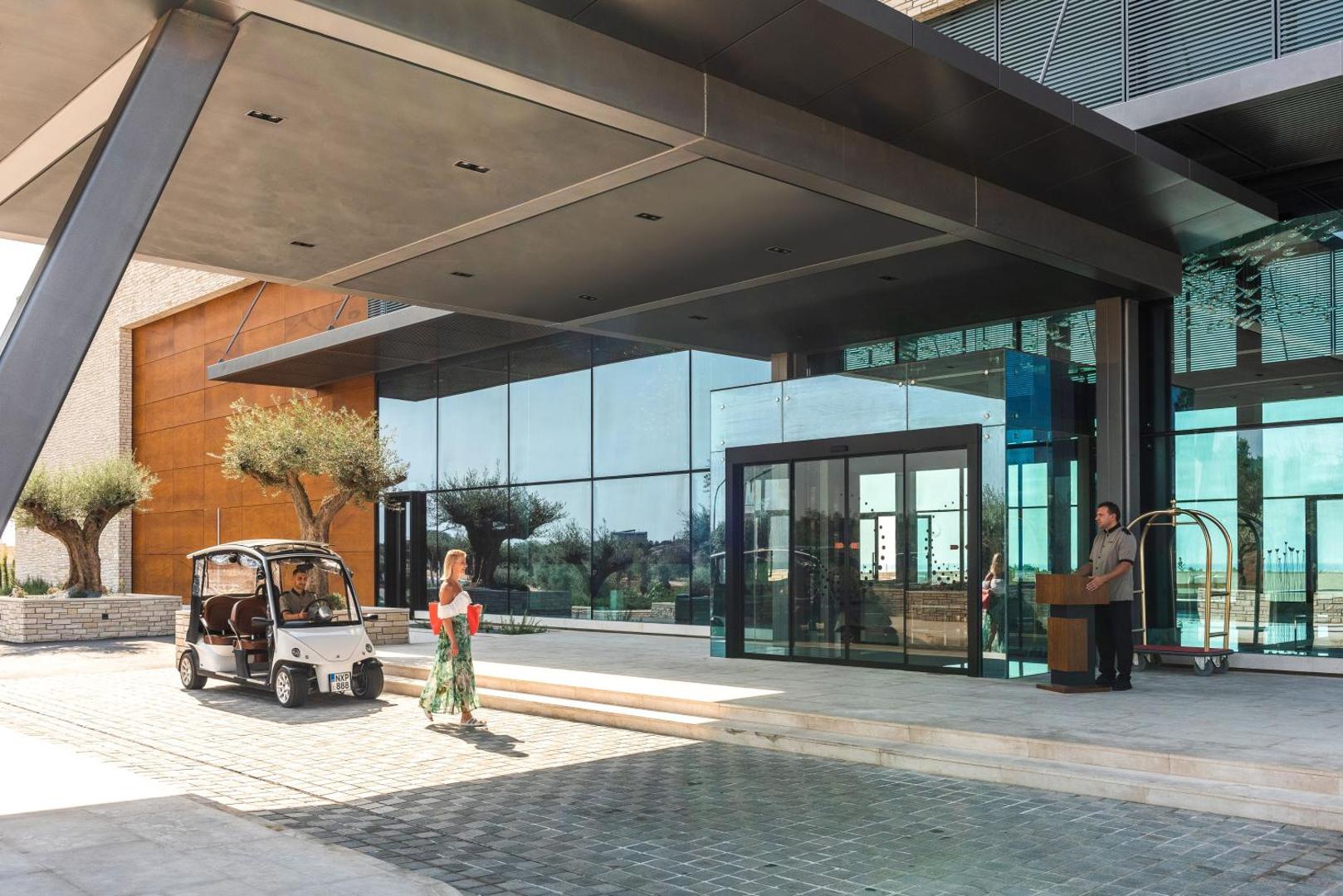 Cap St Georges Hotel & Resort viesu uzņemšanas zona ar golfa auto un konsjerža pakalpojumiem pie modernās stikla ieejas