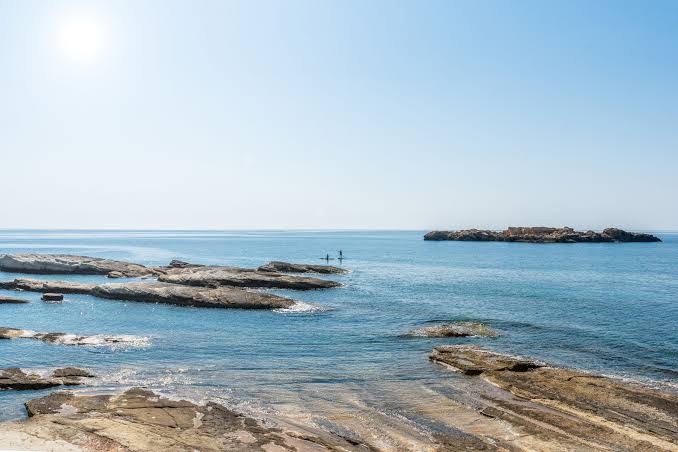Cap St Georges Hotel & Resort akmeņainā piekrastes līnija Kiprā ar skatu uz dzidru jūras ūdeni un nelielu salu tālumā