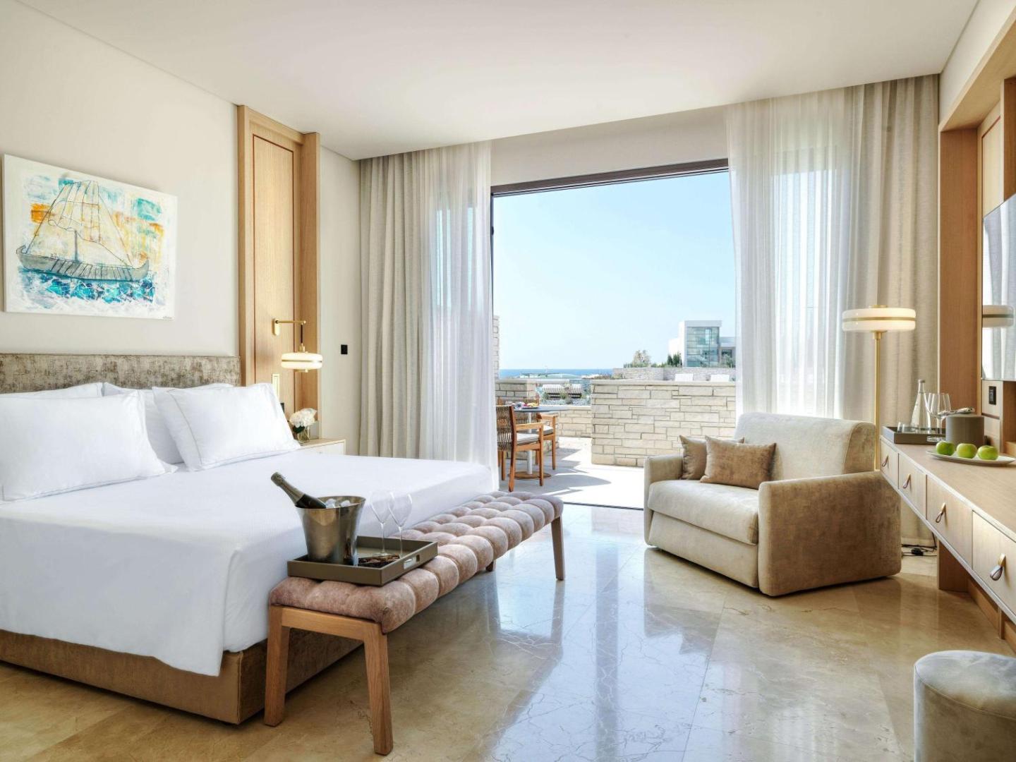 Cap St Georges Hotel & Resort gaišs luksusa numurs ar lielu gultu, atpūtas zonu un skatu uz Vidusjūras piekrasti Kiprā