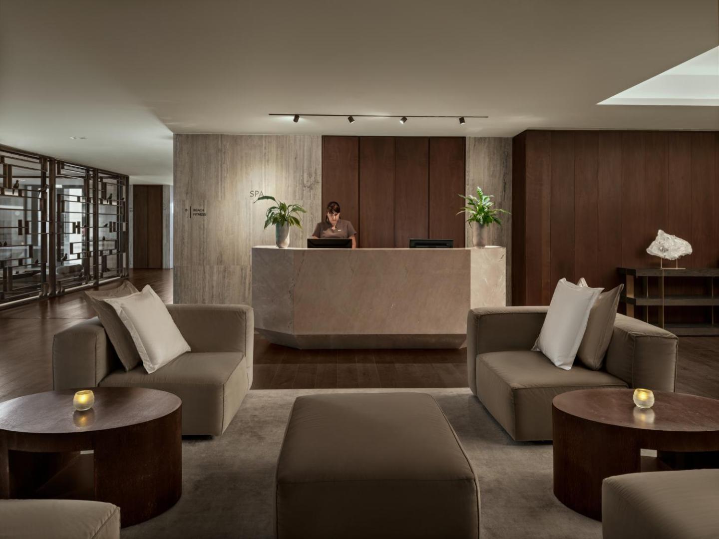 Amara Hotel spa centra recepcija ar akmens leti, mīkstiem atpūtas krēsliem un koka apdari elegantā interjerā