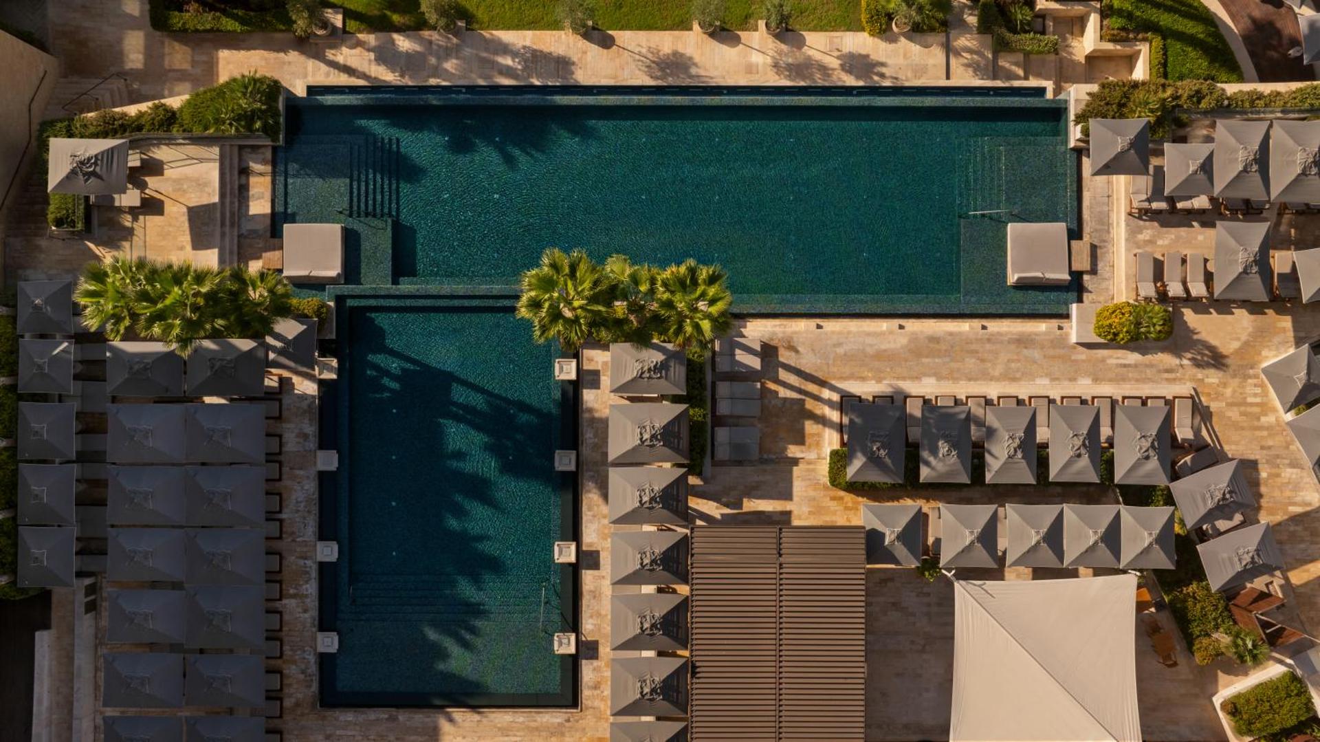 Amara Hotel baseinu zonas skats no augšas — divi taisnstūra formas baseini ar tumši zilu ūdeni, saulessargiem un atpūtas zonām.