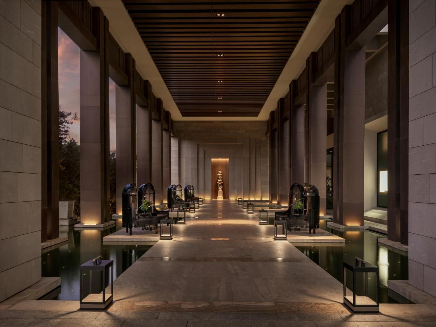 Amara Hotel interjera dizains vakarā — apgaismota eja ar dekoratīviem baseiniem un stilīgiem atpūtas krēsliem
