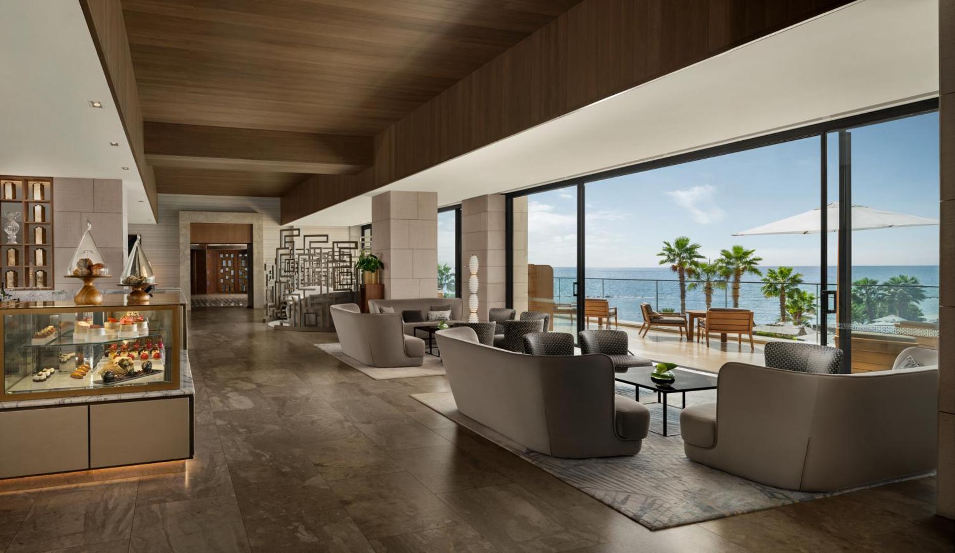 Amara Hotel lobby bārs un atpūtas zona ar panorāmas logiem uz jūru, modernām mēbelēm un konditorejas vitrīnu