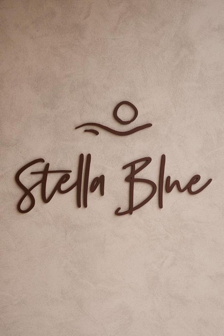 Stella Blue Seaside Resort viesnīcas logo uz teksturētas sienas — minimālistisks dizains brūnos toņos ar saules un viļņu simboliku