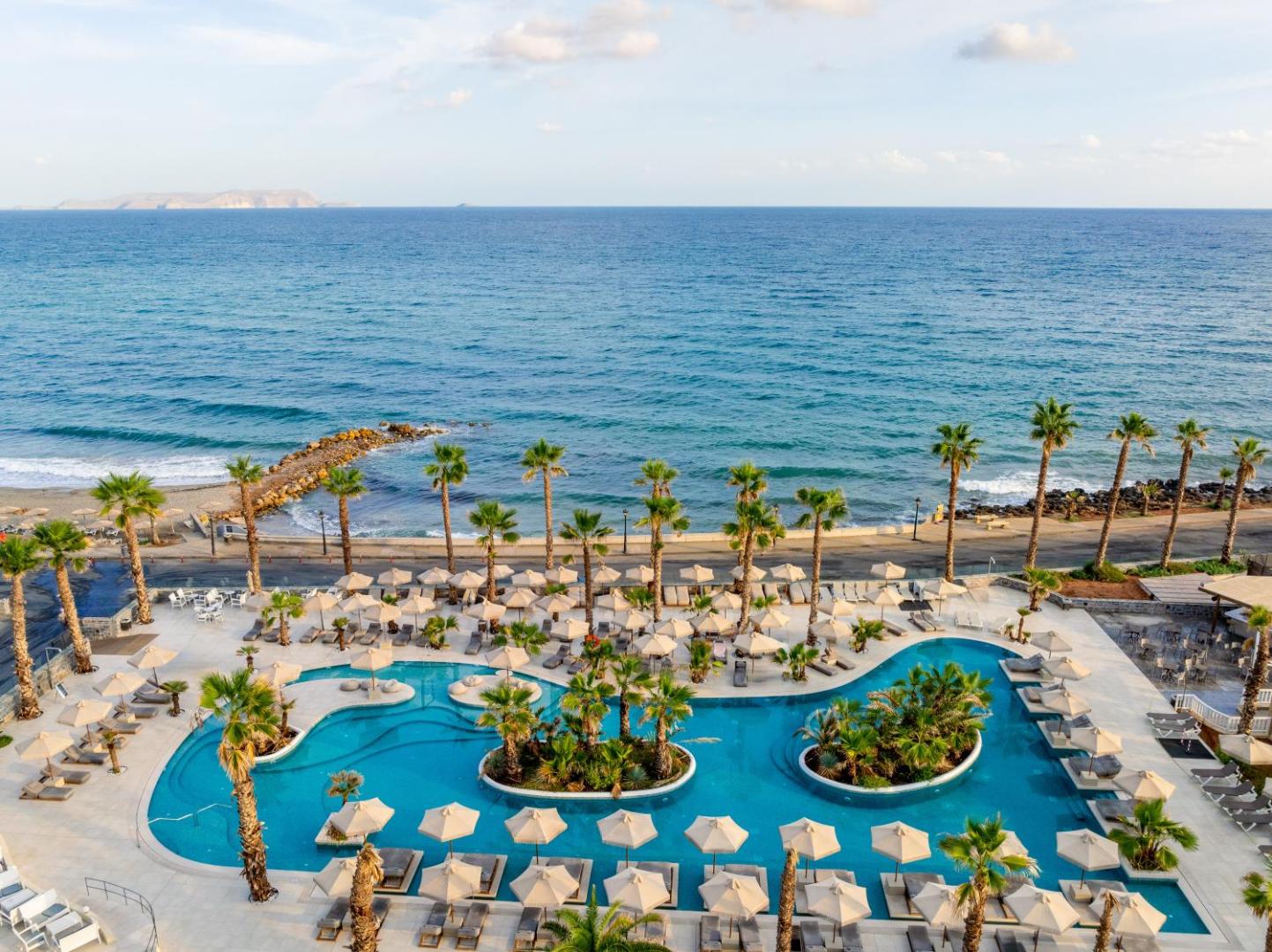 Stella Blue Seaside Resort viesnīcas teritorijas skats no augšas uz baseinu, pludmali un jūras piekrasti ar saulessargiem.
