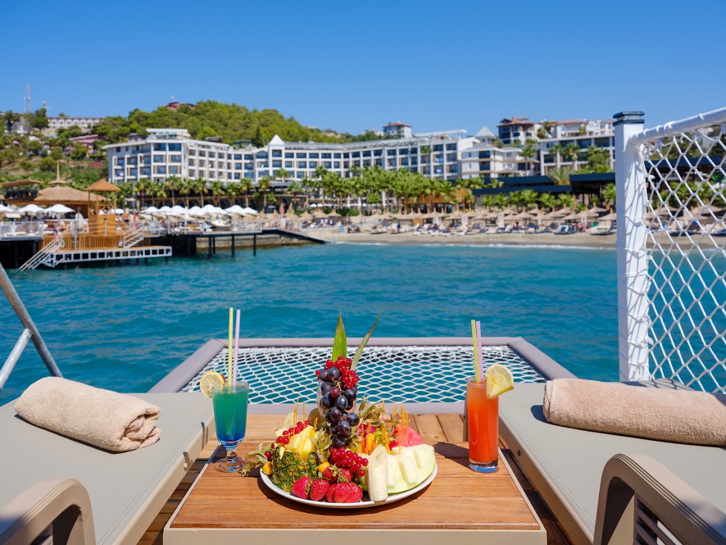 Seven Seas Palmeras Bay skats no privātā mola uz viesnīcu ar augļu plati un kokteiļiem priekšplānā pie Vidusjūras