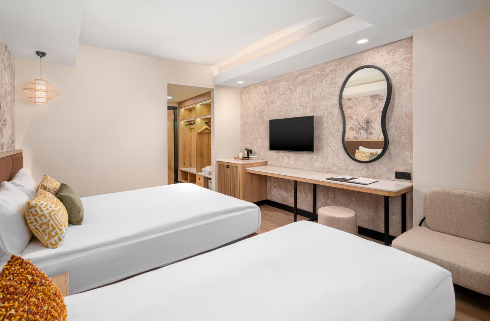 Vox Maris Resort moderns divvietīgs numurs ar gaišām mēbelēm, sienas televizoru un dekoratīvu spoguli Sides reģionā, Turcijā