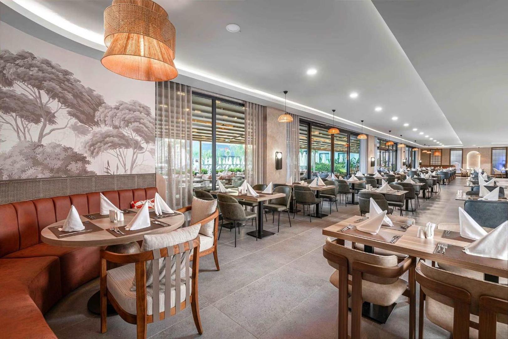 Vox Maris Resort galvenais restorāns ar modernu interjeru, klātiem galdiem un mīkstajiem dīvāniem Sides reģionā, Turcijā