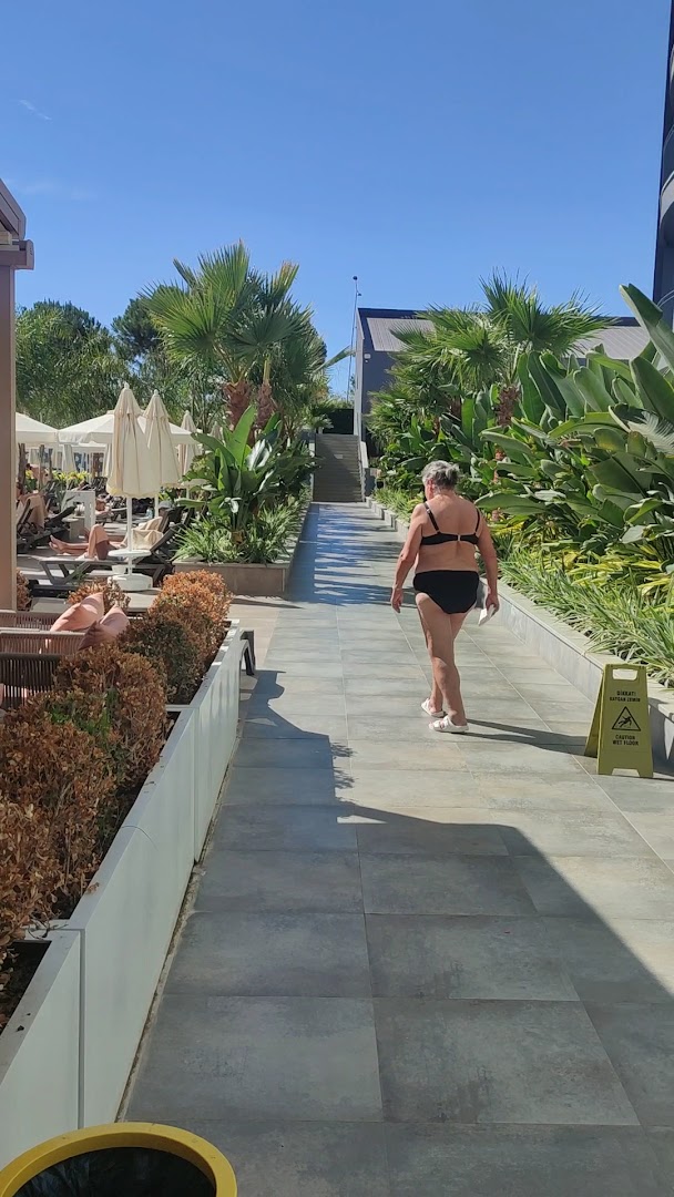 Vox Maris Resort āra teritorija ar flīzētu gājēju celiņu, palmām un sauļošanās zonu ar saulessargiem pie baseina