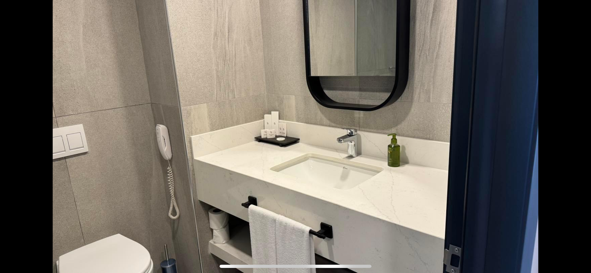 Vox Maris Resort numura vannasistaba ar gaišu marmora virsmu, modernu izlietni, spoguli un higiēnas piederumiem