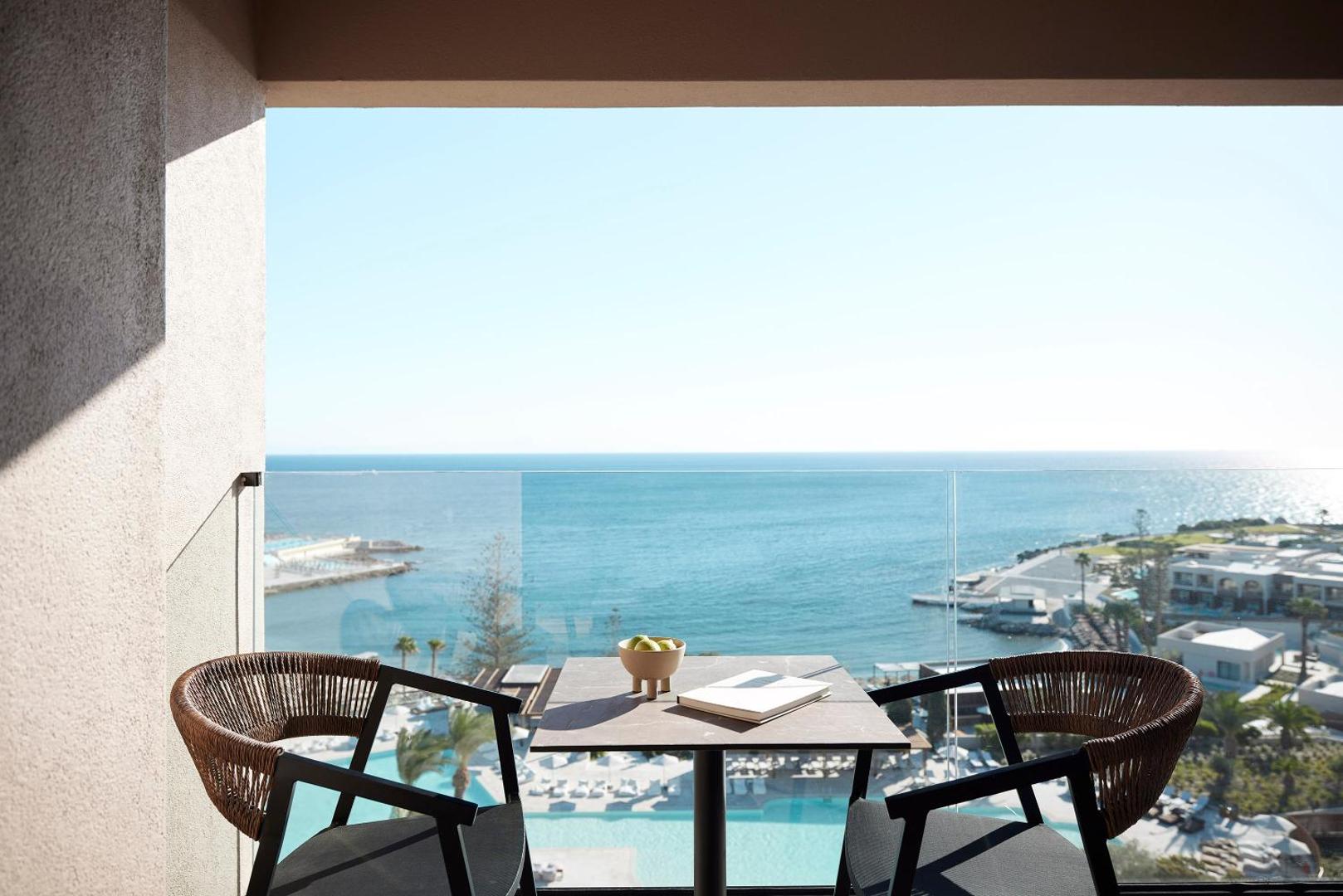 Skats no Helea Lifestyle Beach Resort balkona uz Rodas piekrasti — galdiņš diviem, stiklota marga un skats uz kūrorta teritoriju